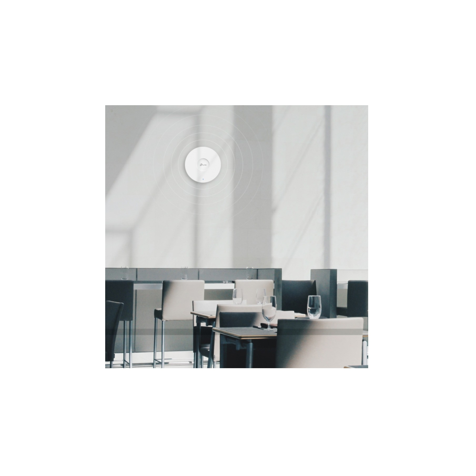 Biały punkt dostępowy TP-Link na ścianie, z okręgami światła wokół, w otoczeniu restauracji.