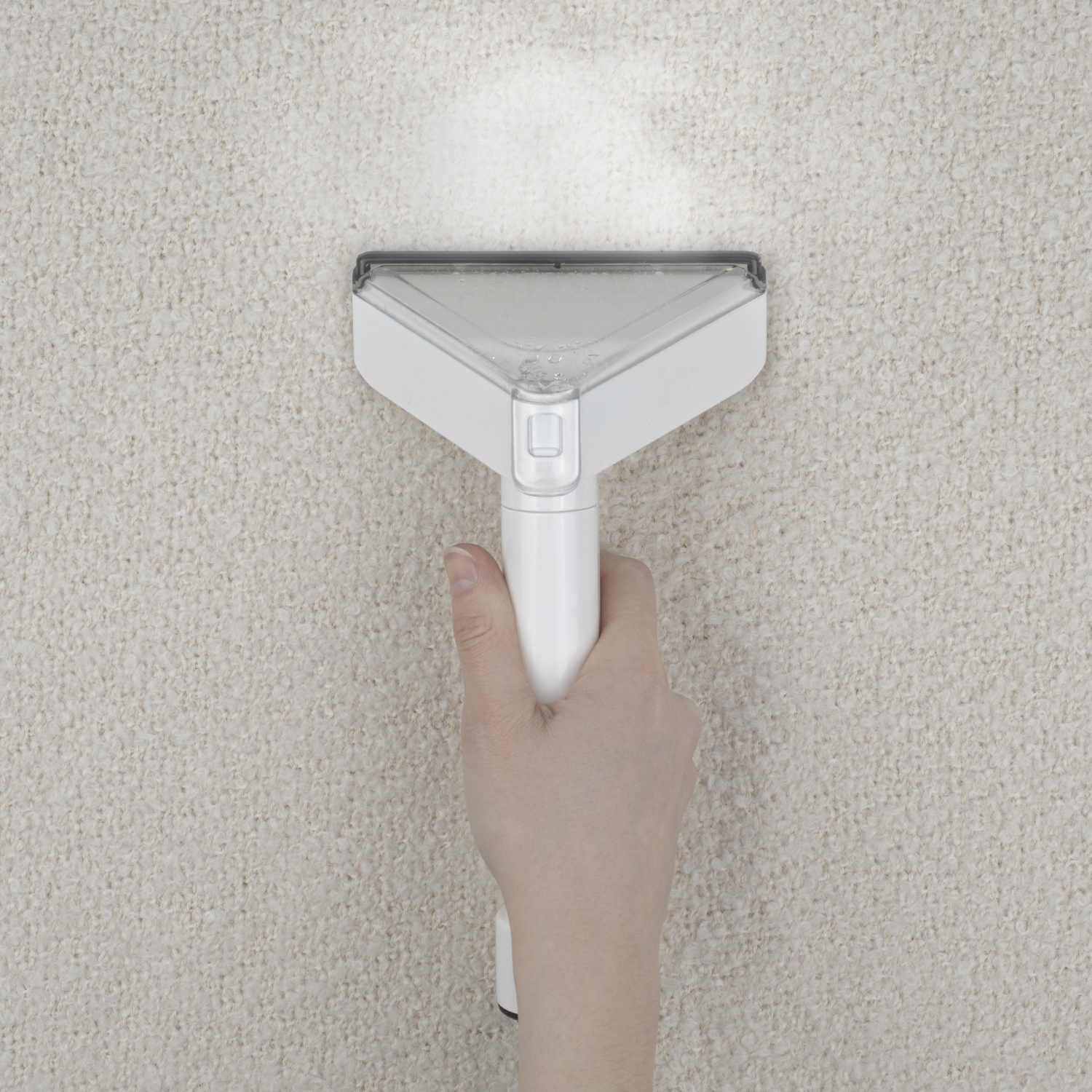 Una mano usando una herramienta de limpieza blanca en una alfombra estampada.