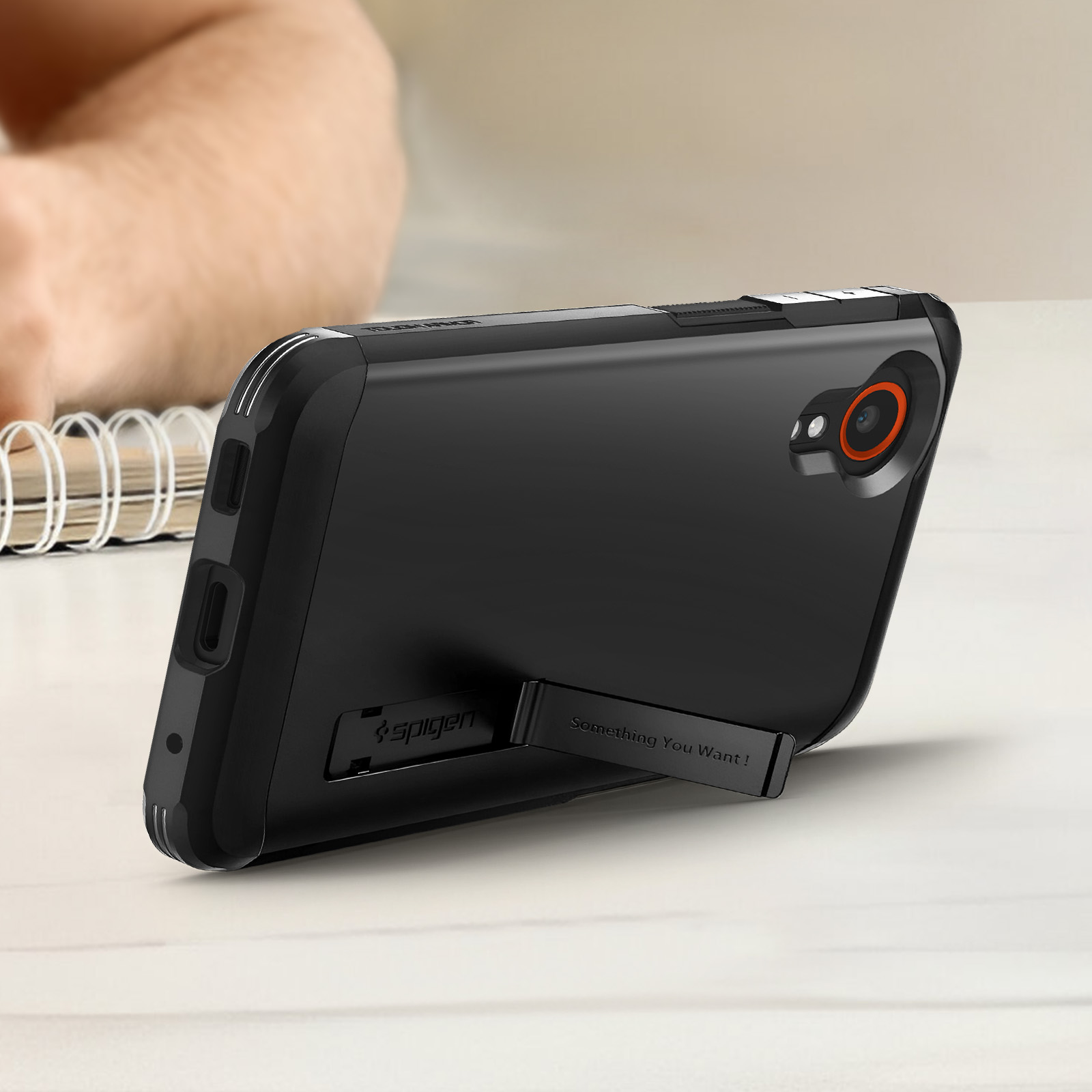 Coque de téléphone noire sur une surface en bois blanc. La main d'une personne est floue en arrière-plan.