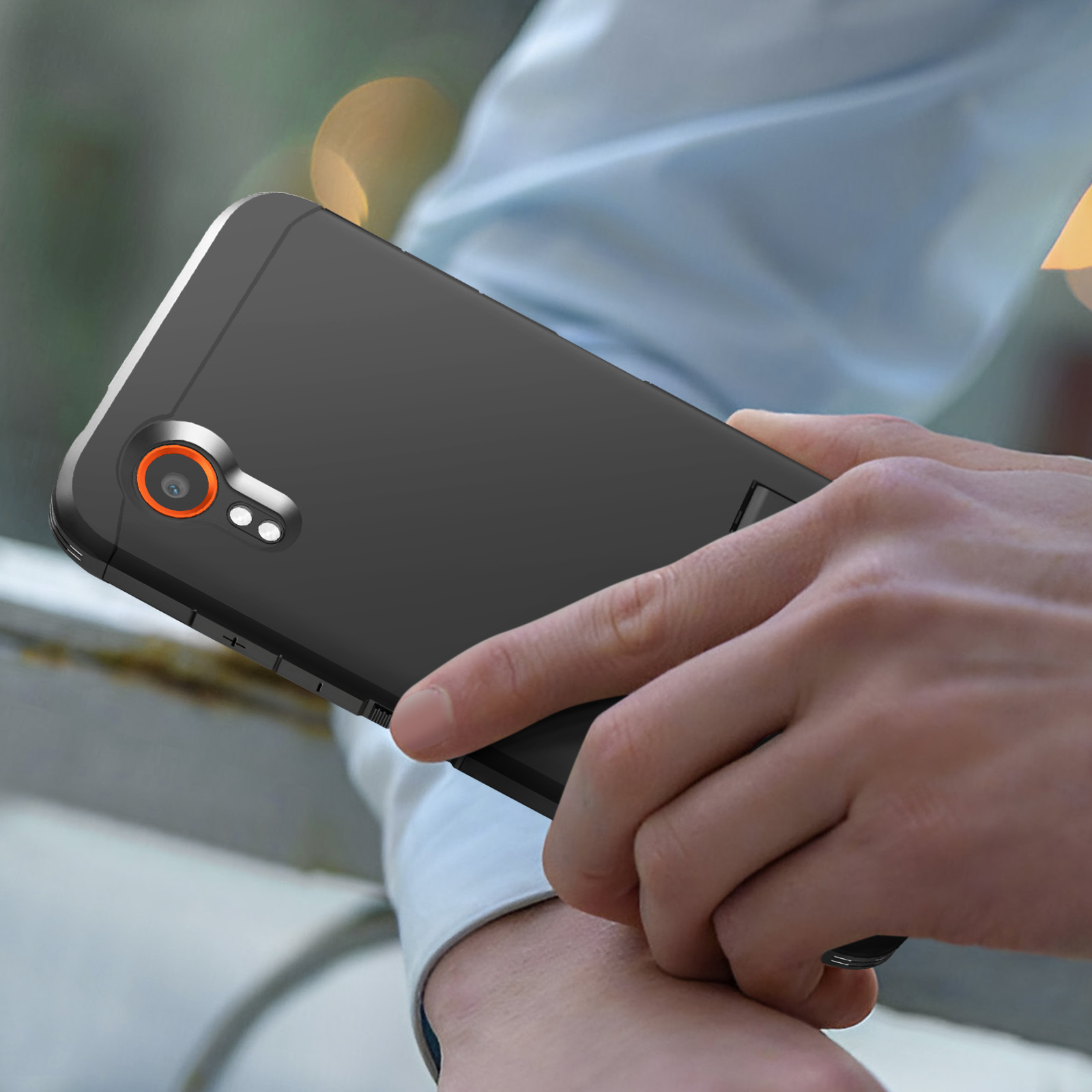 Une main tenant un smartphone noir avec un anneau de caméra orange.