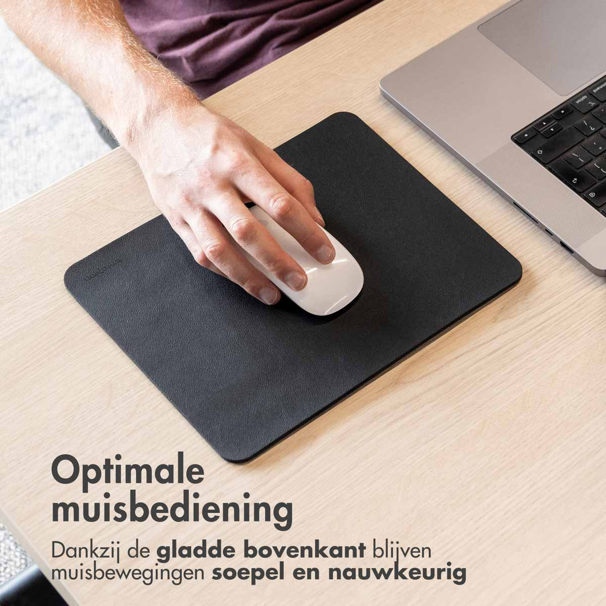 Hand using a white mouse on a black mousepad, with a laptop in the background.