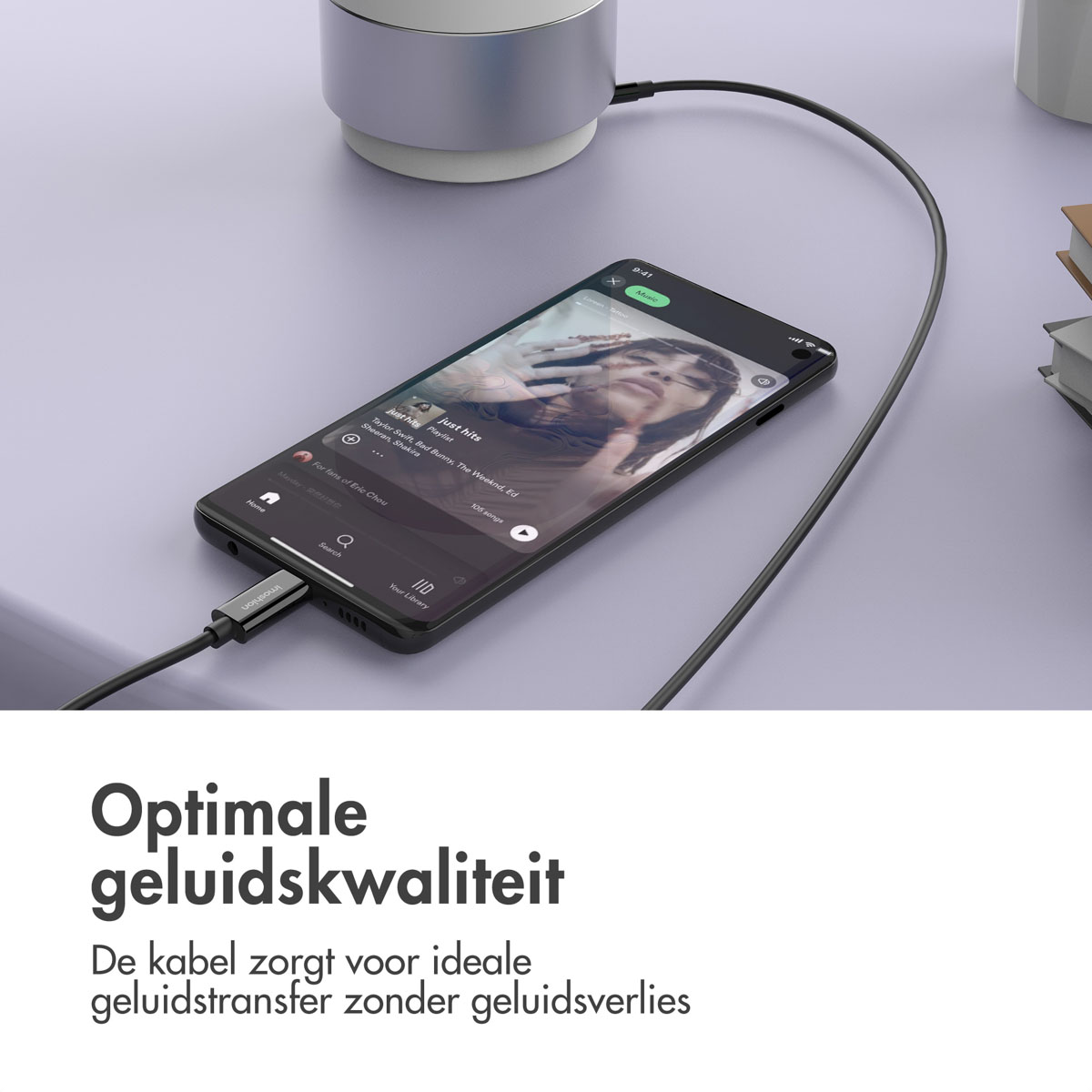 Een telefoon is aangesloten op een luidspreker. Een zwarte kabel is aangesloten op de telefoon. De scène is binnen.