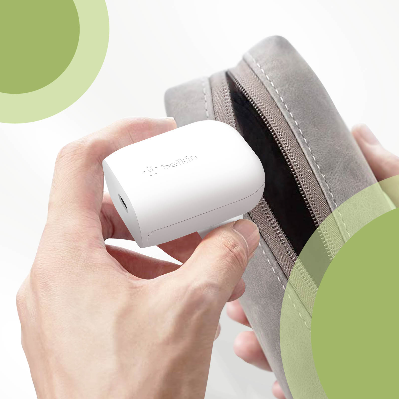 Una mano tiene un caricatore Belkin bianco, accanto a una custodia grigia con zip.