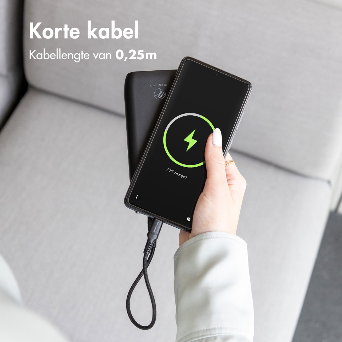 Une personne tenant un téléphone en charge. Une banque d'alimentation est à côté. Le texte dit 'Korte kabel'.