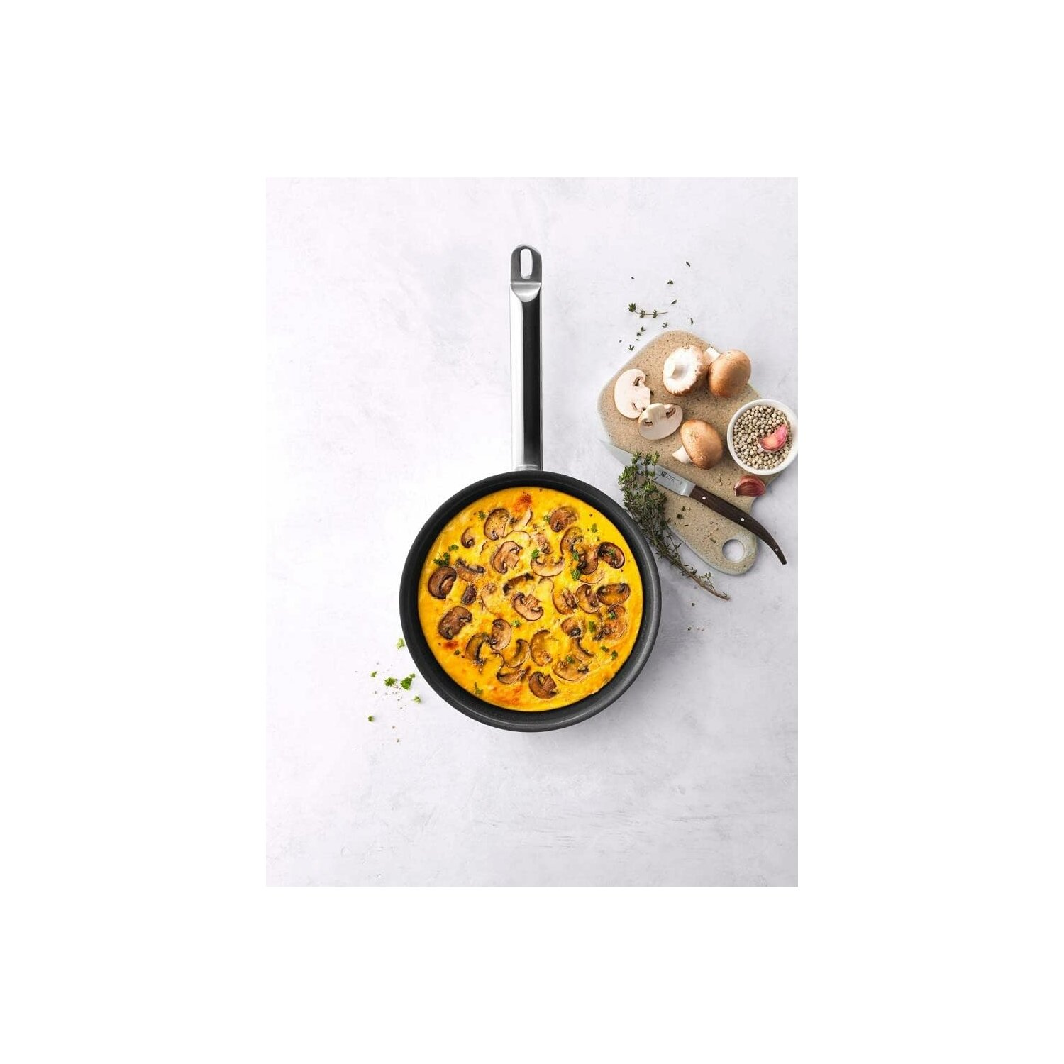 Una padella con una frittata con funghi sopra, accanto a un tagliere con ingredienti.