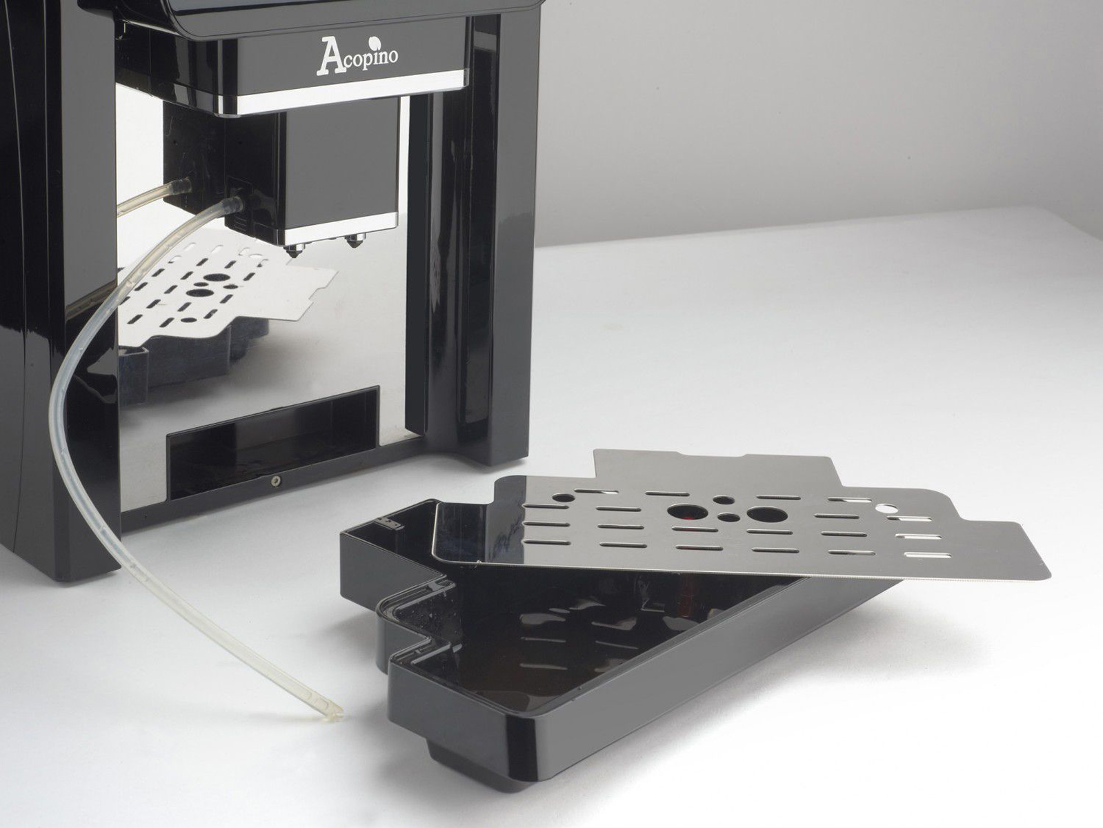 Czarny ekspres do kawy ze srebrnymi elementami. Taca jest wysunięta. Tło jest białe.