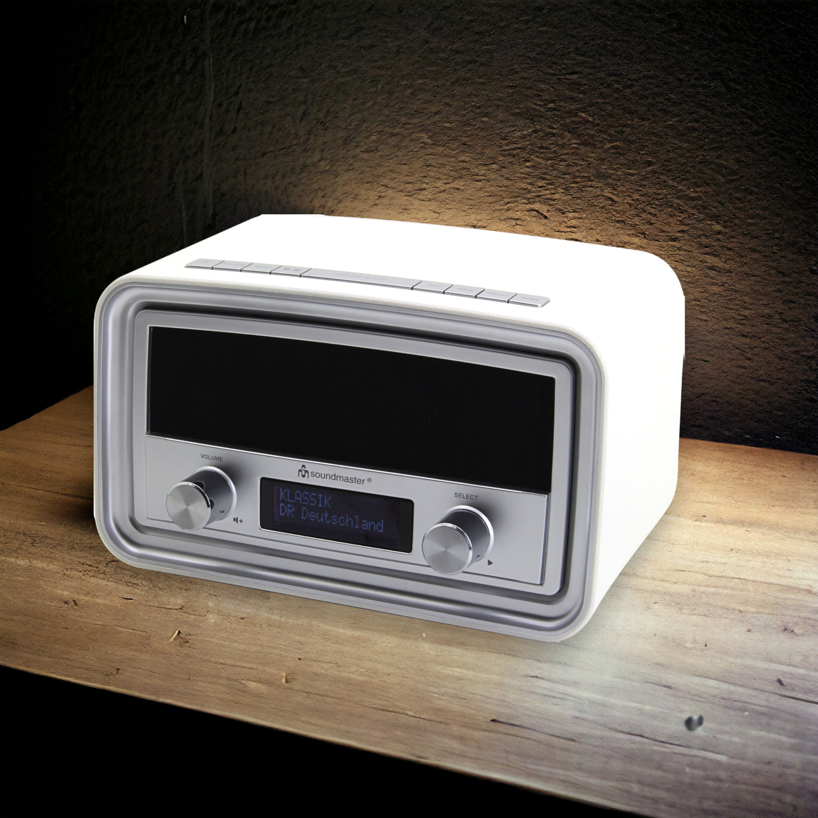Weißes Radio mit Knöpfen und Knöpfen auf Holz, schwarzes Display. Dunkler Wandhintergrund.