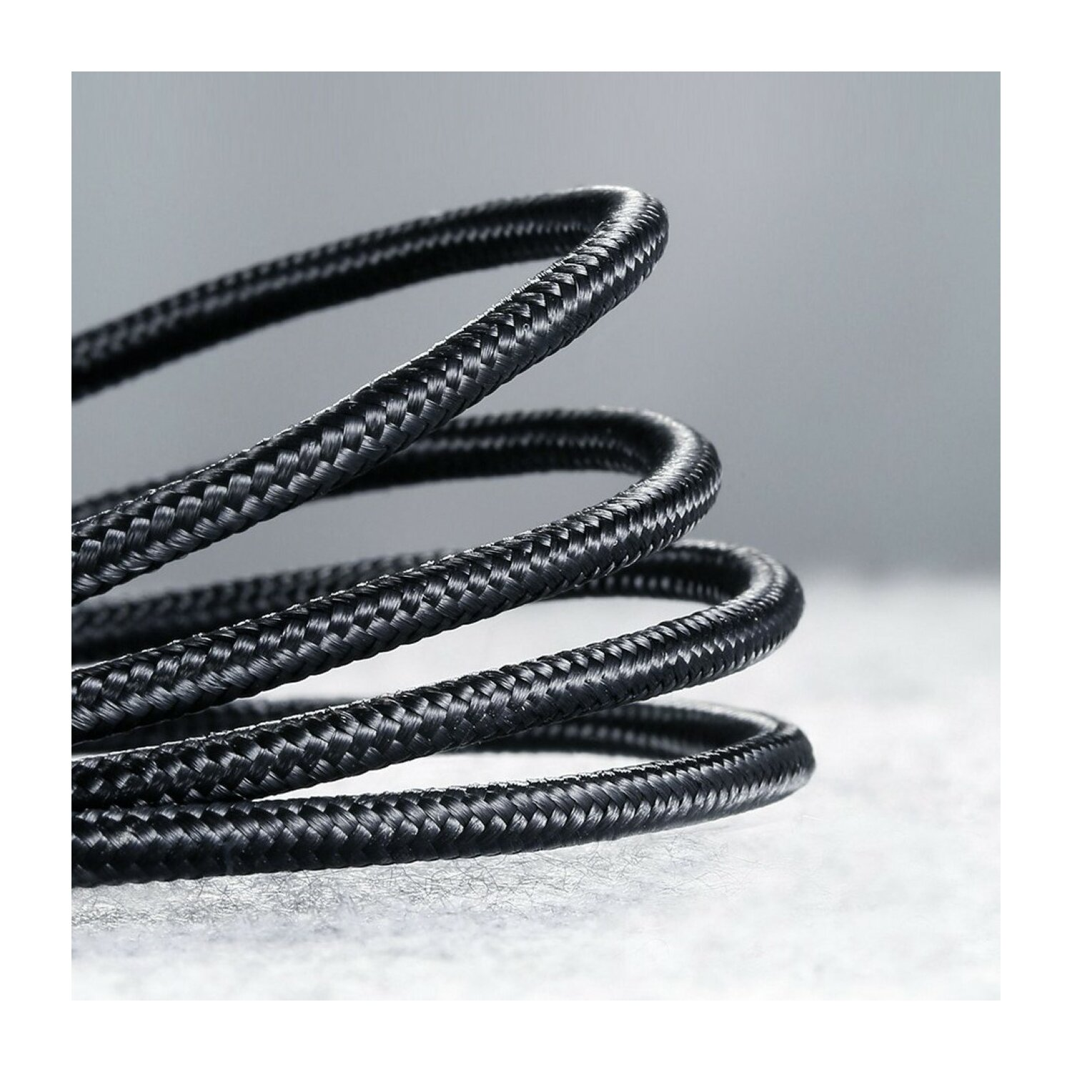 Zbliżenie czarnego plecionego kabla, spiralnie zwiniętego. Szare tło.