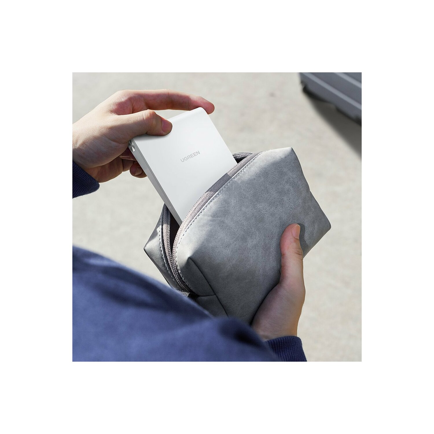 Hände einer Person, die einen grauen Beutel mit einer weißen UGREEN Powerbank halten.