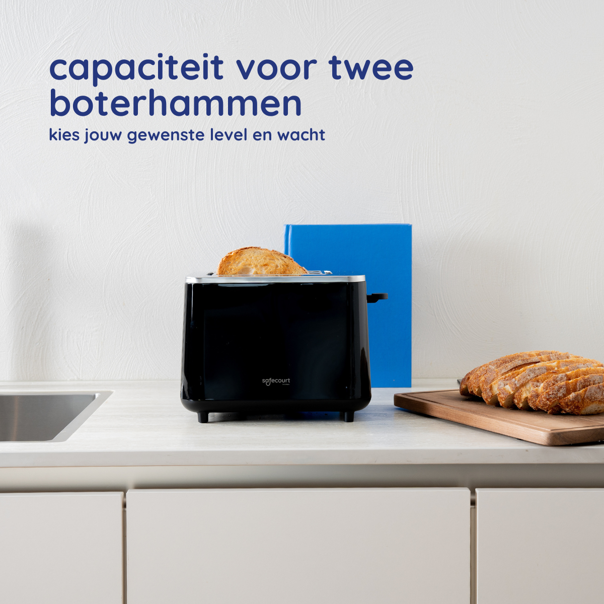Zwarte broodrooster met brood erin, wit aanrecht, houten snijplank met sneetjes brood en een blauw blok.