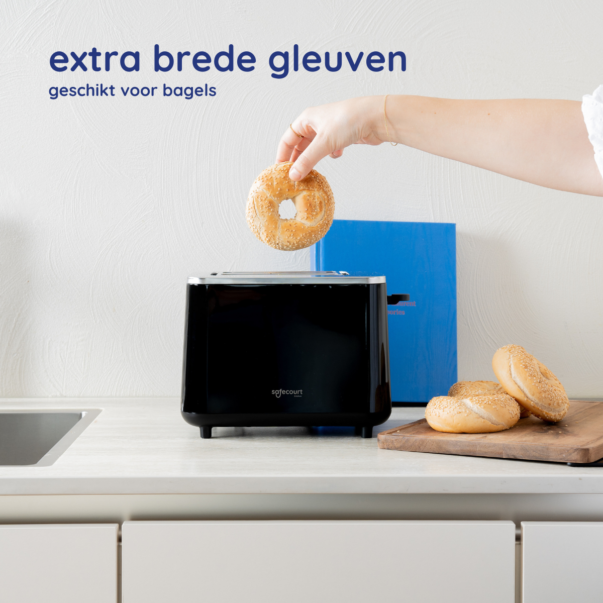 Een zwarte broodrooster met een bagel die erin wordt geplaatst. Twee bagels op een houten plank zijn zichtbaar.