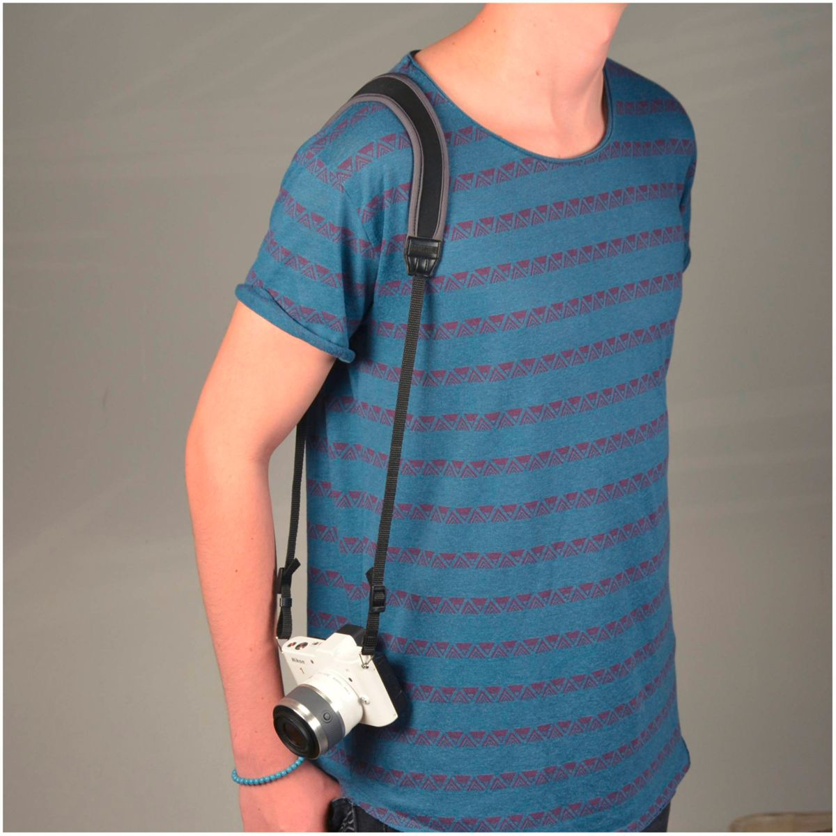 Osoba w niebieskiej koszuli z aparatem na szyi, na szarym tle.