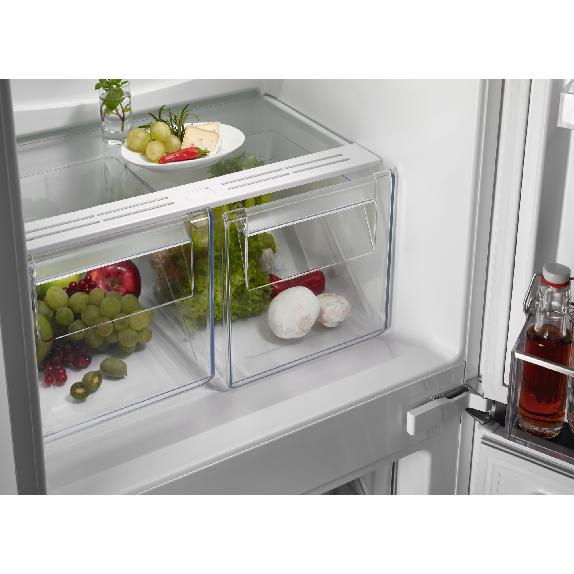 Interior del refrigerador con frutas y verduras en los cajones. Botellas y frascos de vidrio también son visibles.