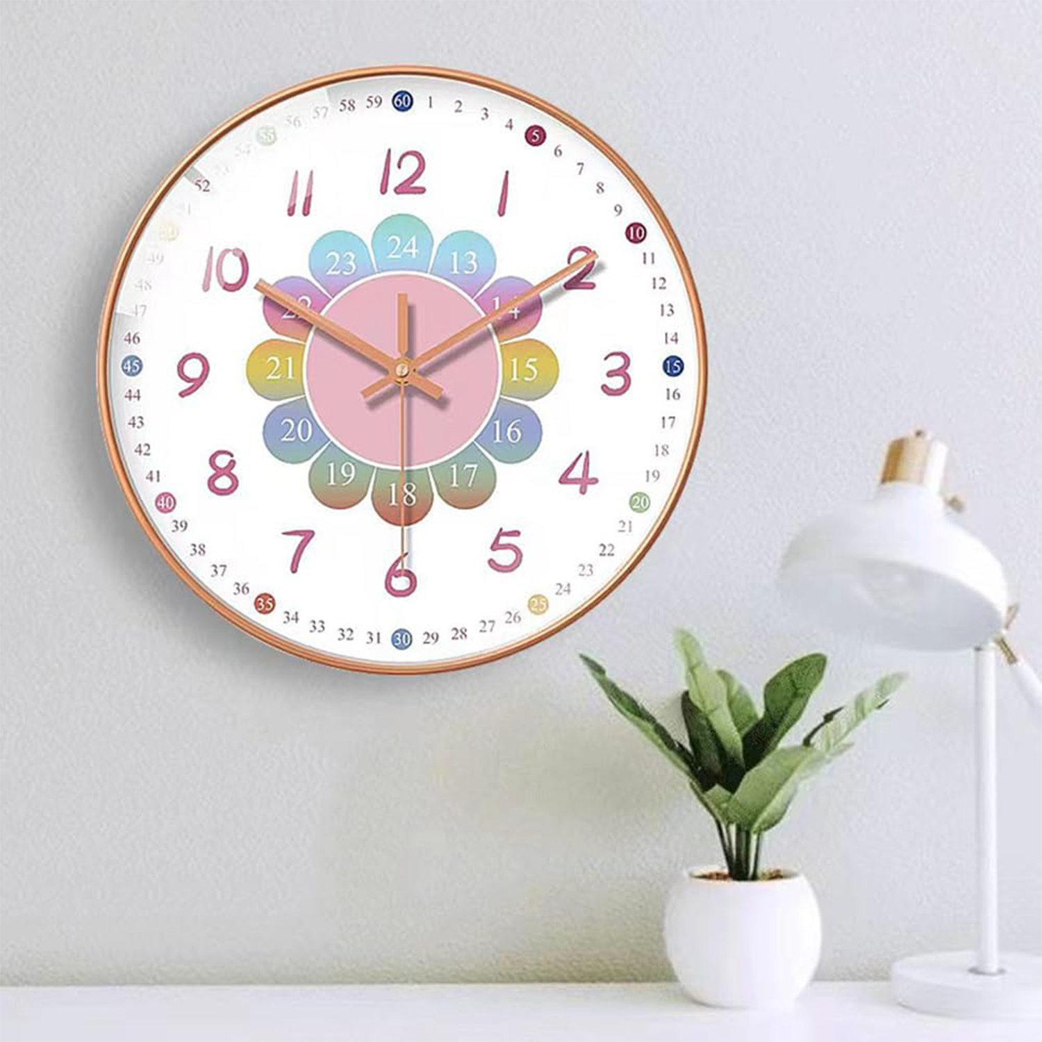 Eine Wanduhr mit Blumendesign, Zahlen und Zeigern. Auf einer weißen Oberfläche stehen eine Pflanze und eine Lampe.