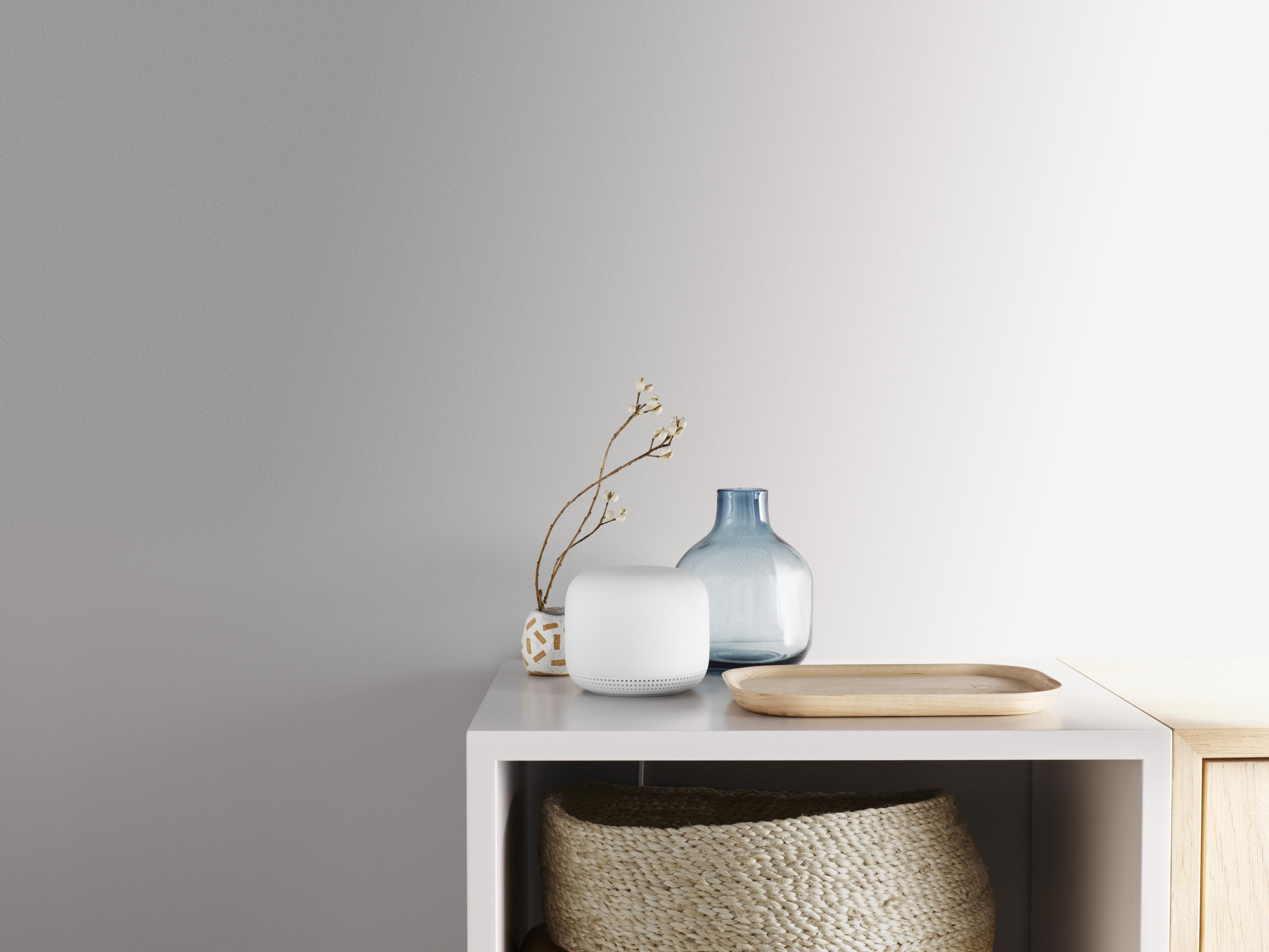 Biała półka z białym głośnikiem, niebieskim wazonem i drewnianą tacą.