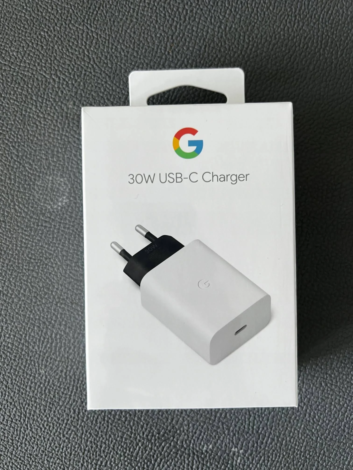 Un cargador USB-C Google de 30W blanco en su caja, visto desde una perspectiva a la altura de los ojos.
