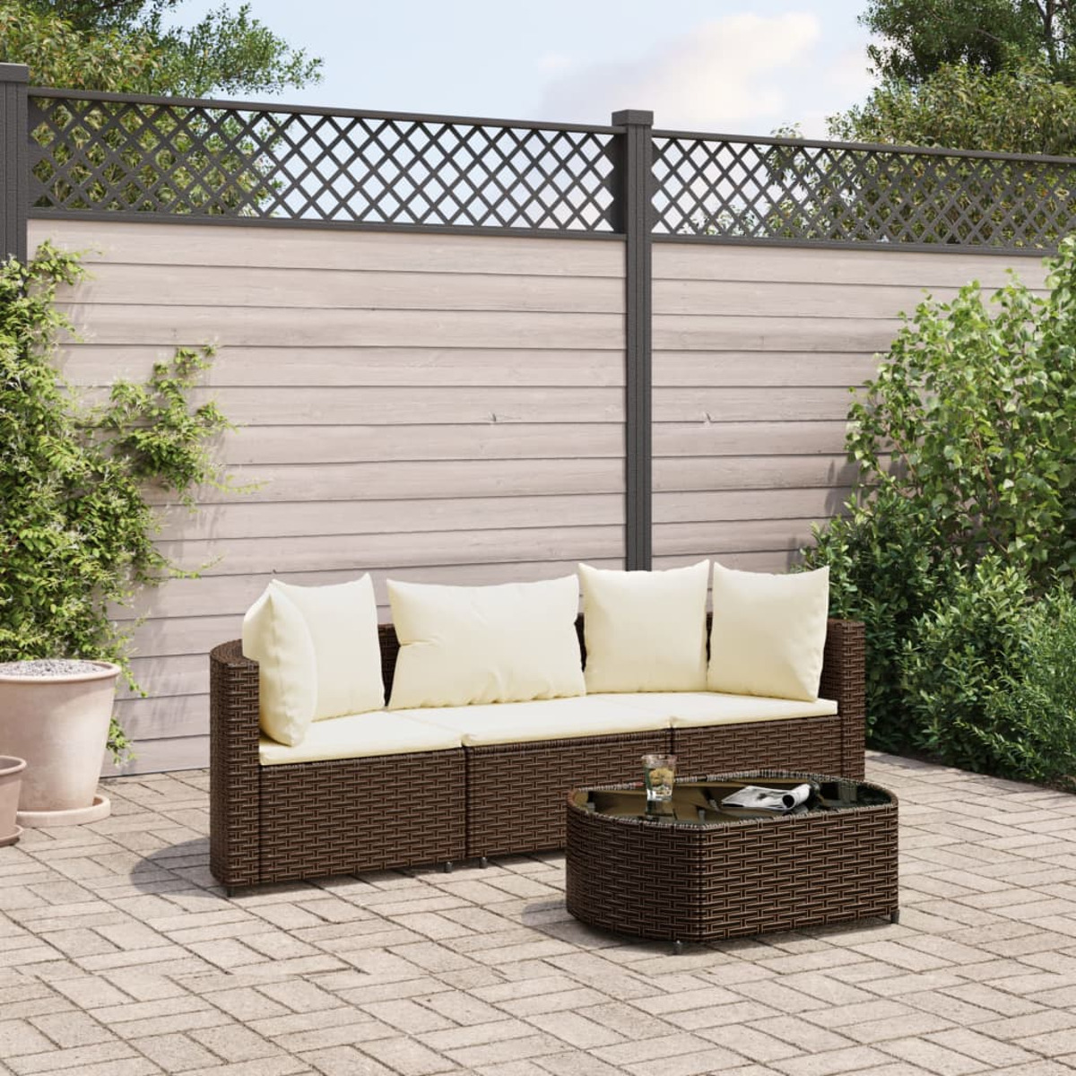 Ein braunes Outdoor-Wicker-Sofaset mit cremefarbenen Kissen und einem Tisch mit Glasplatte. Hintergrund ist ein Zaun.