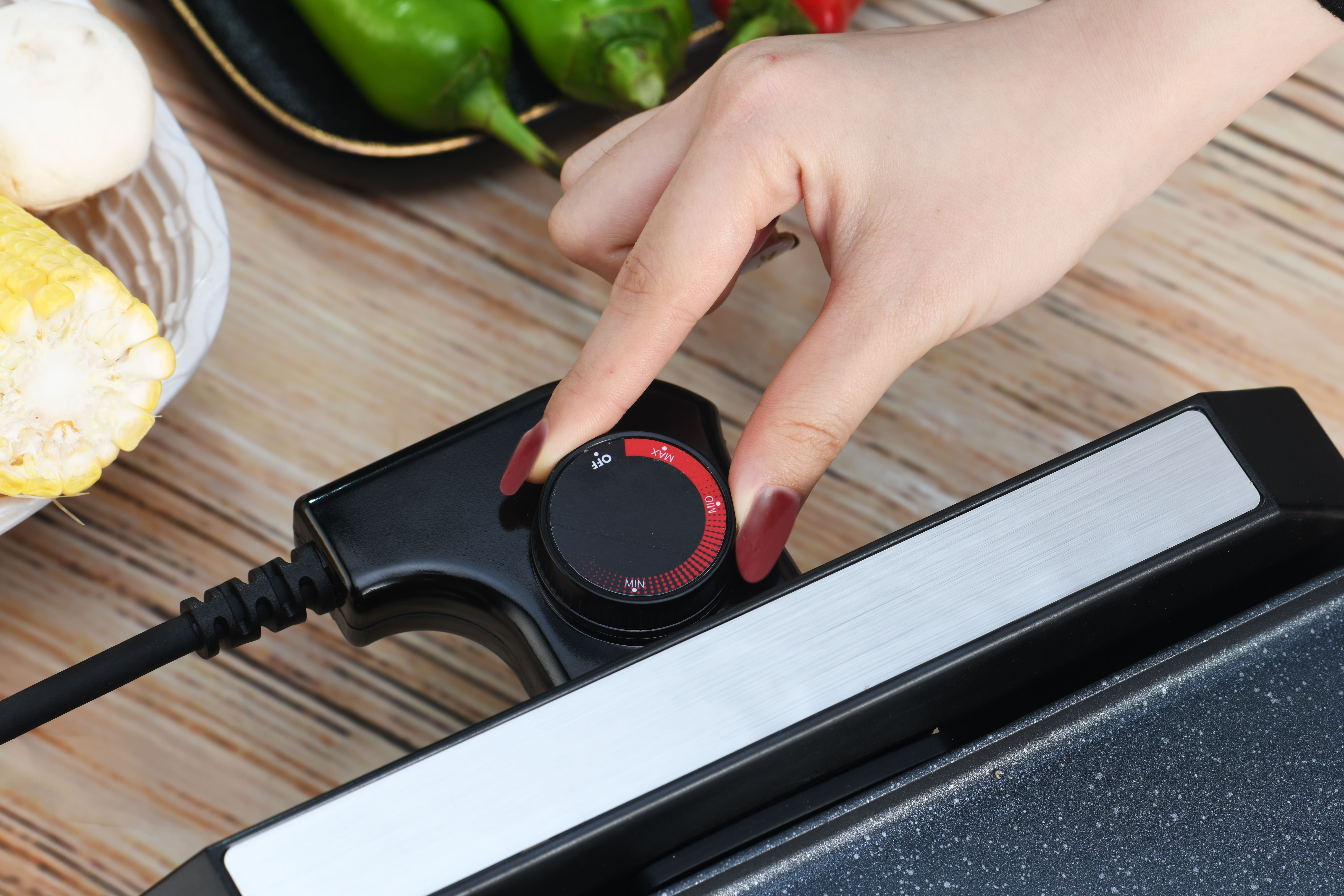 Eine Hand, die den Temperaturregler an einem schwarzen Grill einstellt.