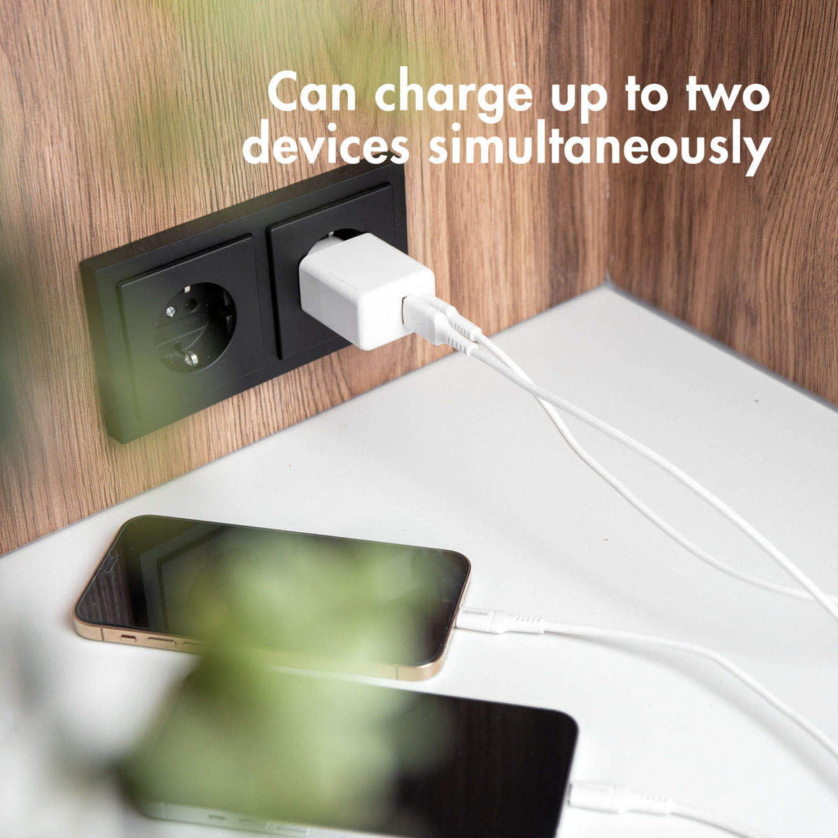 Twee telefoons opladen met witte kabels en een zwart stopcontact.