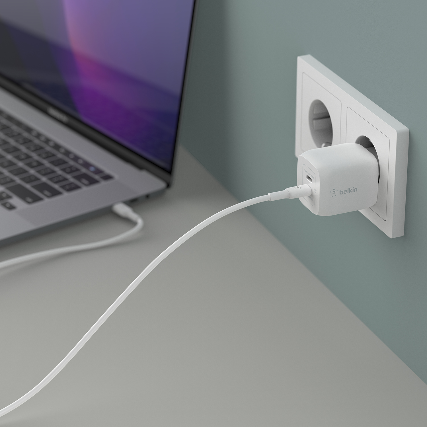 Laptop mit Ladekabel, das an ein Belkin-Ladegerät angeschlossen ist, das an einer Steckdose angeschlossen ist.