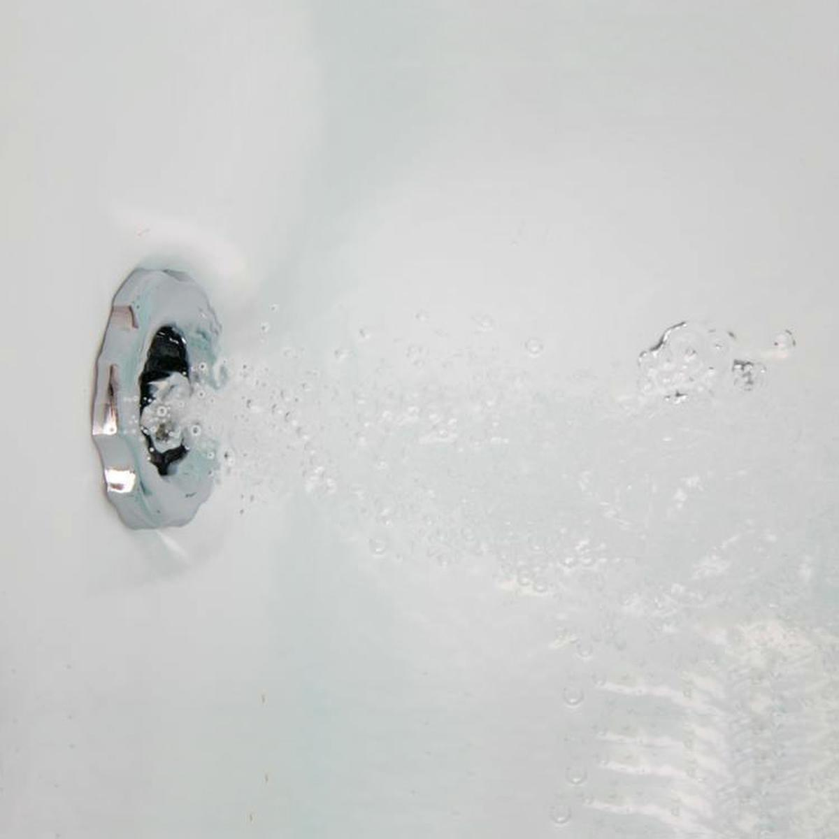 Nahaufnahme eines verchromten Wasserstrahls in einer weißen Badewanne mit Wasser und Blasen.