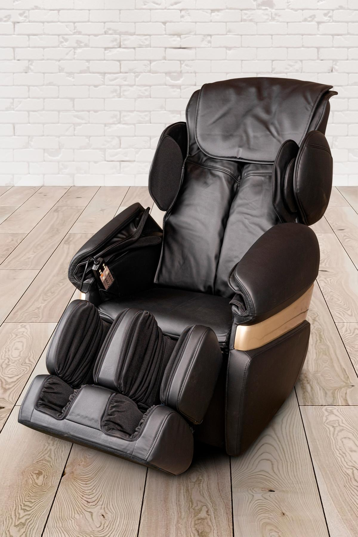Ein schwarzer Massagesessel mit Holzboden und weißem Backsteinhintergrund. Er befindet sich in Liegeposition.