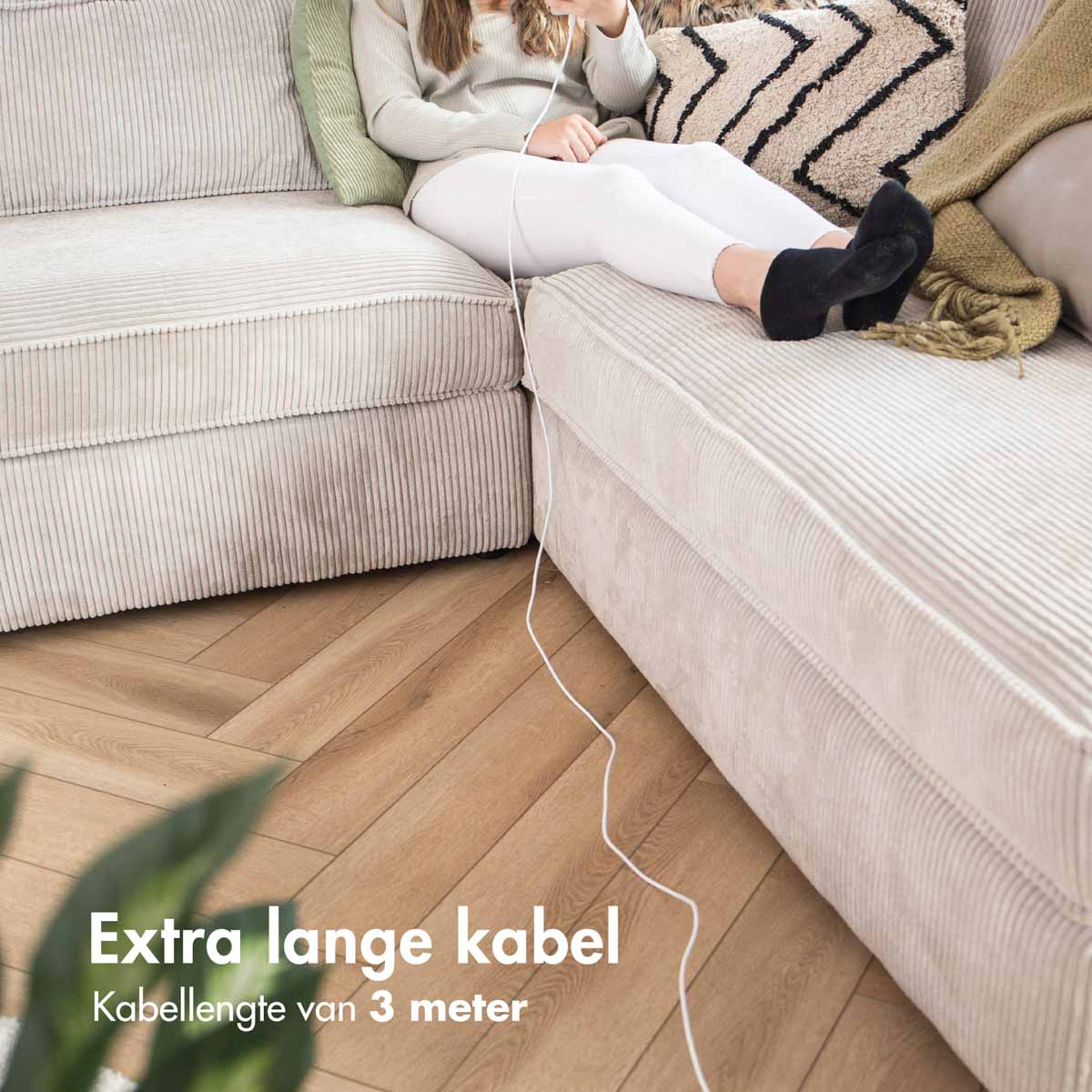 Femme assise sur un canapé en velours côtelé beige, chargeant son téléphone avec un câble.