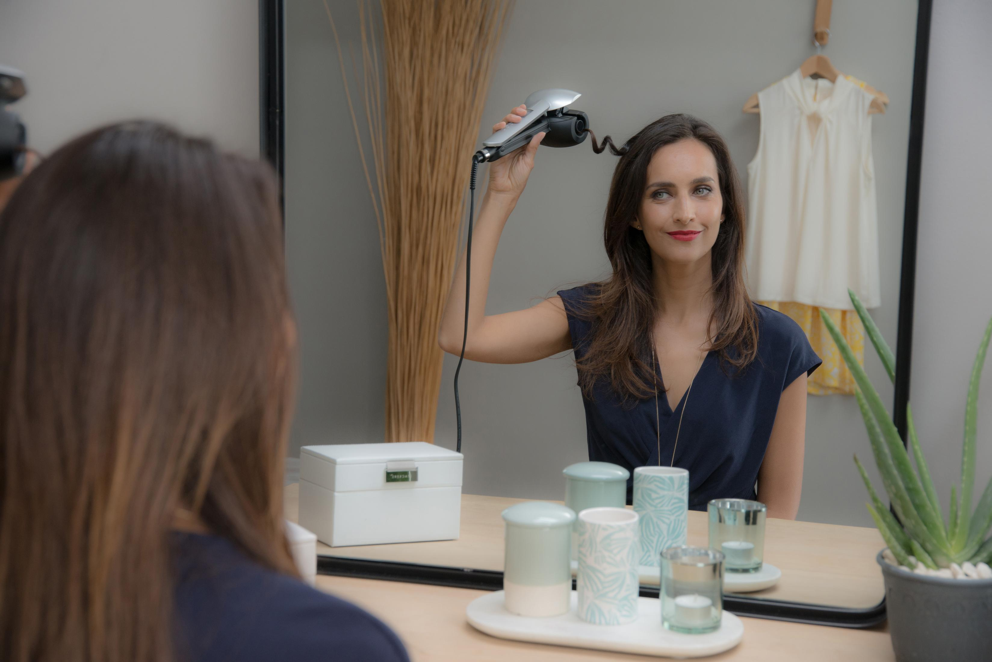 Kobieta używająca lokówki w lustrze.