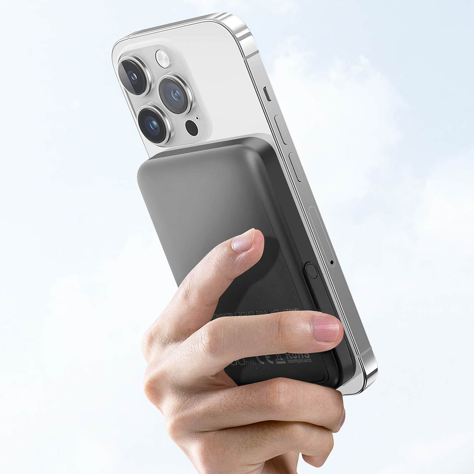 Une main tenant une batterie externe noire attachée à un téléphone blanc. Le fond est le ciel.