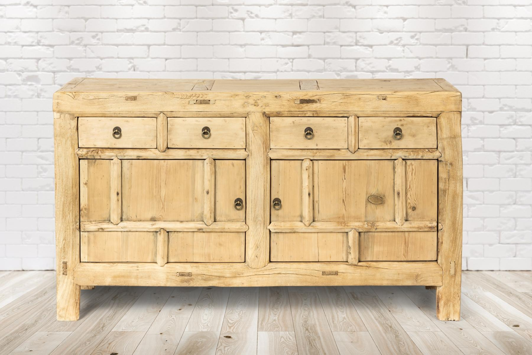 Ein hellbrauner Holzschrank mit Schubladen und Türen vor einem weißen Ziegelmauer-Hintergrund.