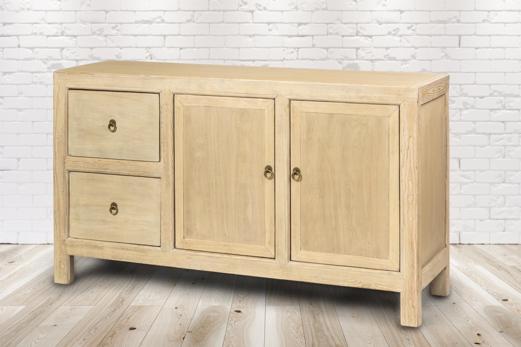 Hellholzschrank mit zwei Schubladen und zwei Türen, Messingknöpfen, auf Holzboden, weißer Backstein-Hintergrund.