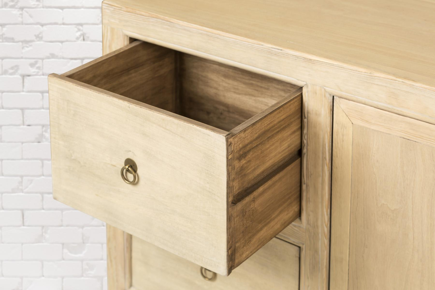 Ein Holzschrank mit einer geöffneten Schublade, die das Innere zeigt, vor einem Hintergrund aus weißen Ziegeln.