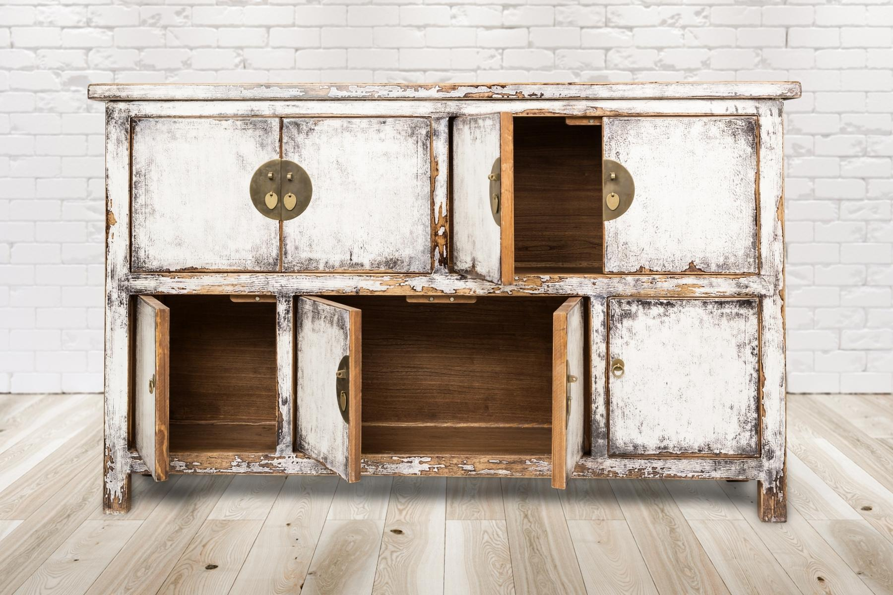 Ein abgenutzter weißer Holzschrank mit offenen Türen, auf einem Holzboden.