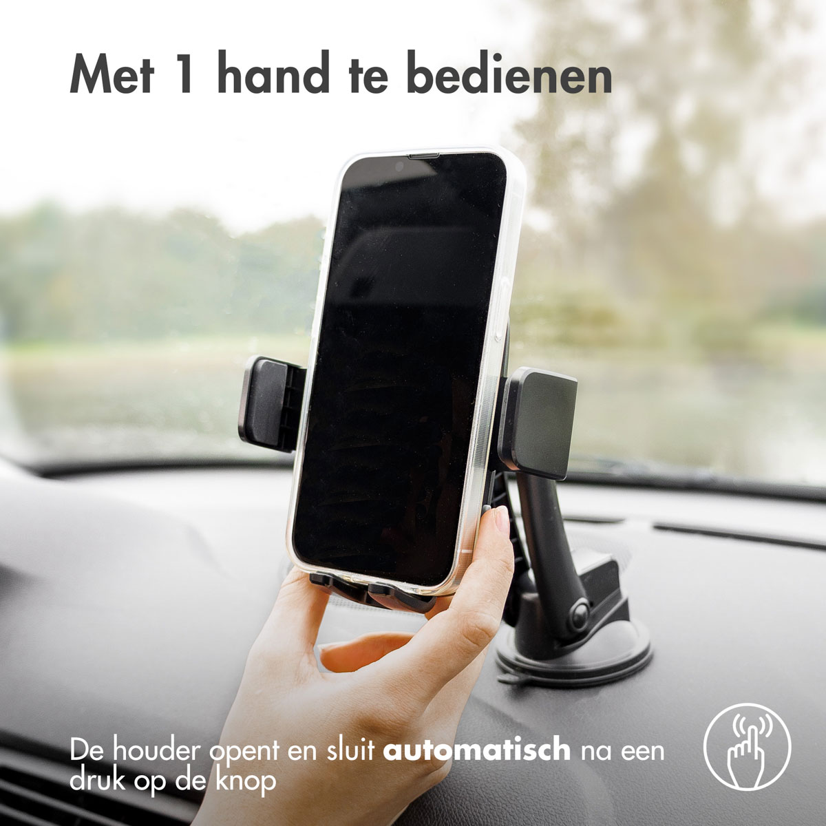 A phone in a car mount. The mount is black with a suction cup. A hand is holding the phone.