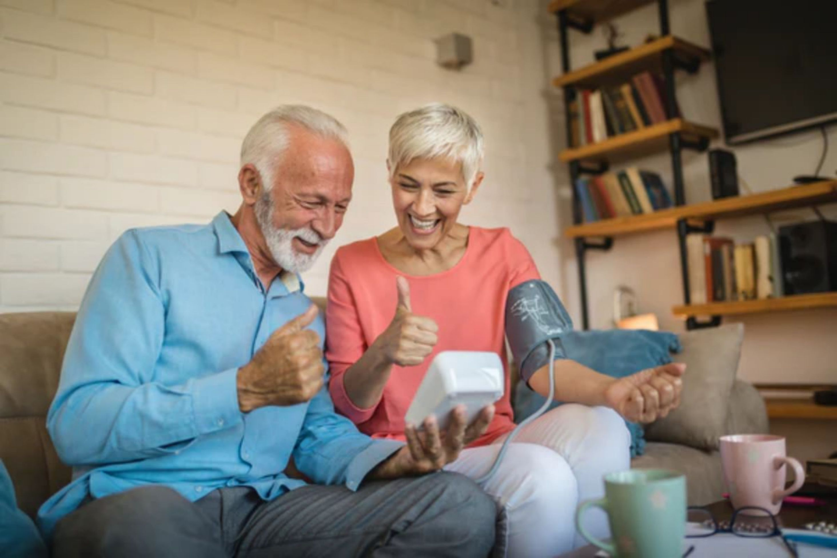 Un couple de personnes âgées regardant joyeusement un tensiomètre, pouces levés.