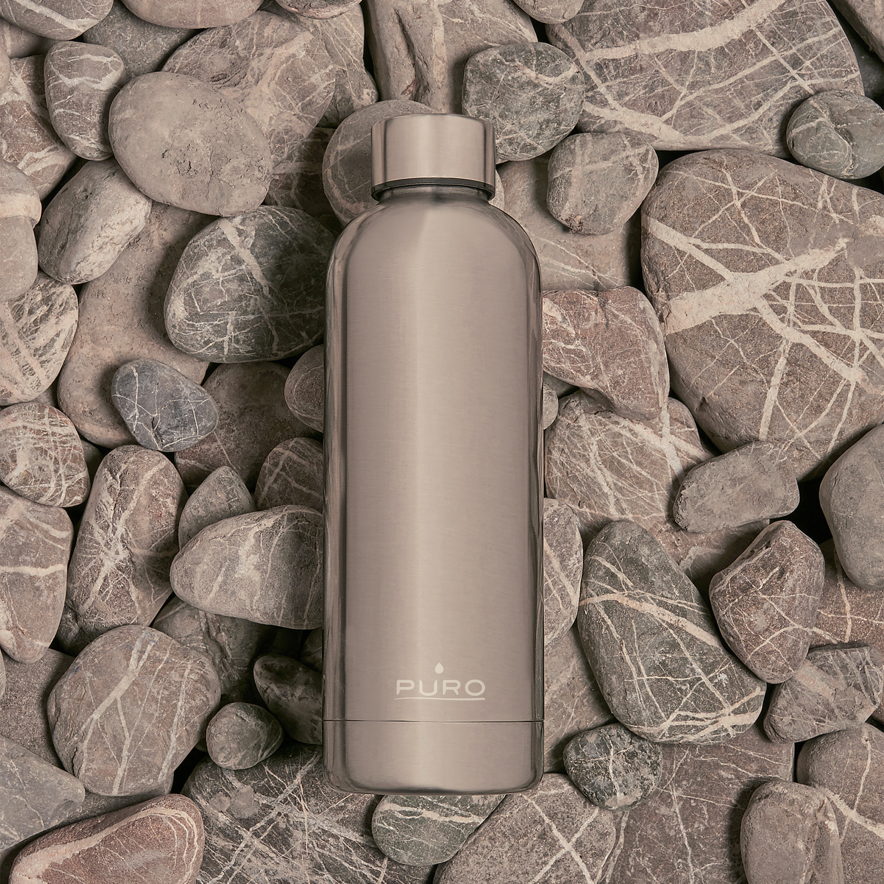 Una botella de agua de acero inoxidable sobre un lecho de rocas grises, con la palabra 'PURO'.
