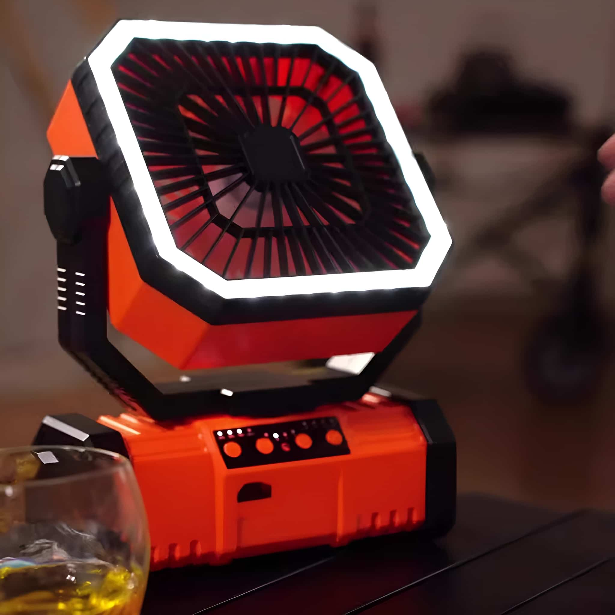 Ein orange-schwarzer Ventilator mit Licht, steht auf einem Tisch neben einem Glas.