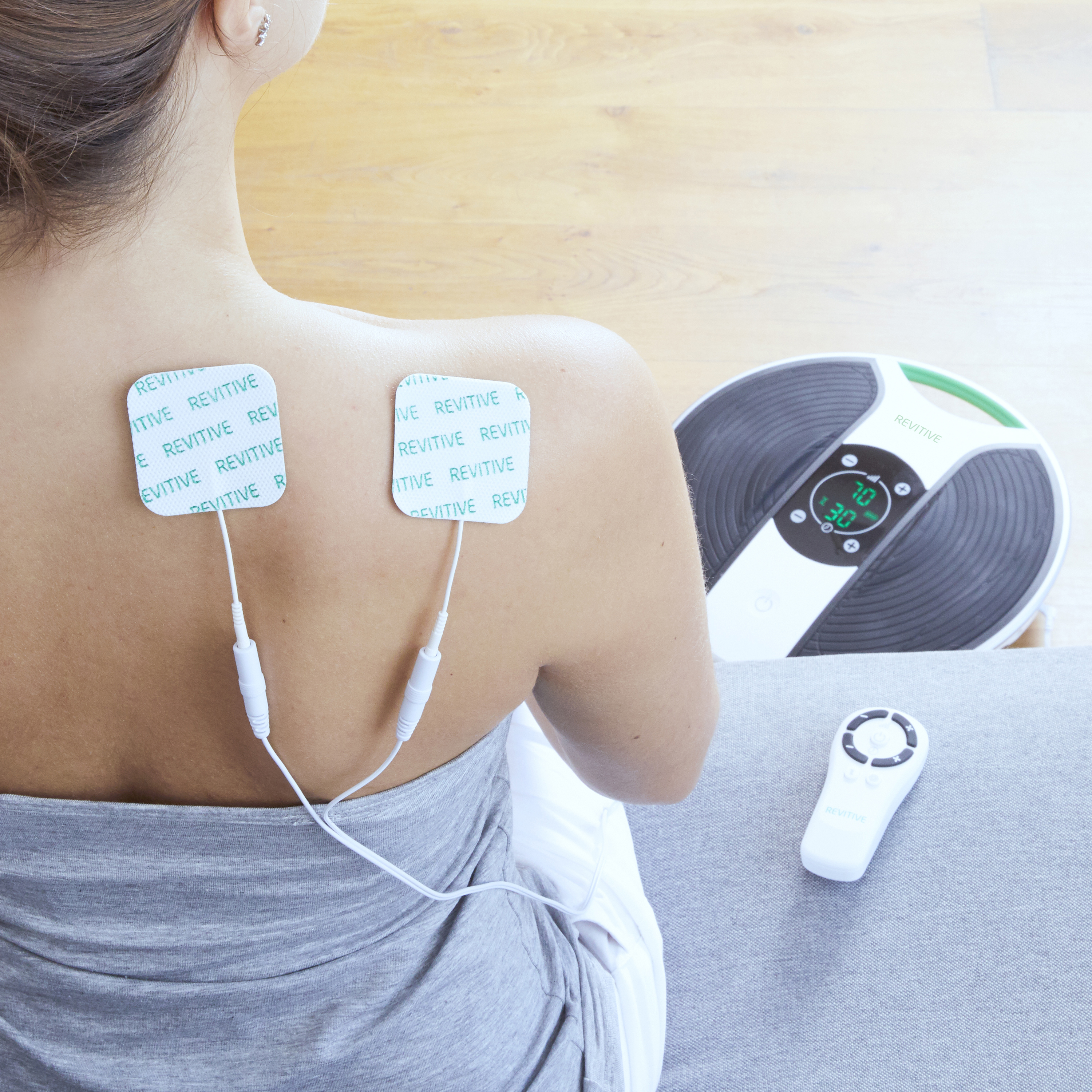 Eine Frau hat Elektrodenpads auf dem Rücken. Ein Gerät steht rechts. Eine Fernbedienung liegt darunter.