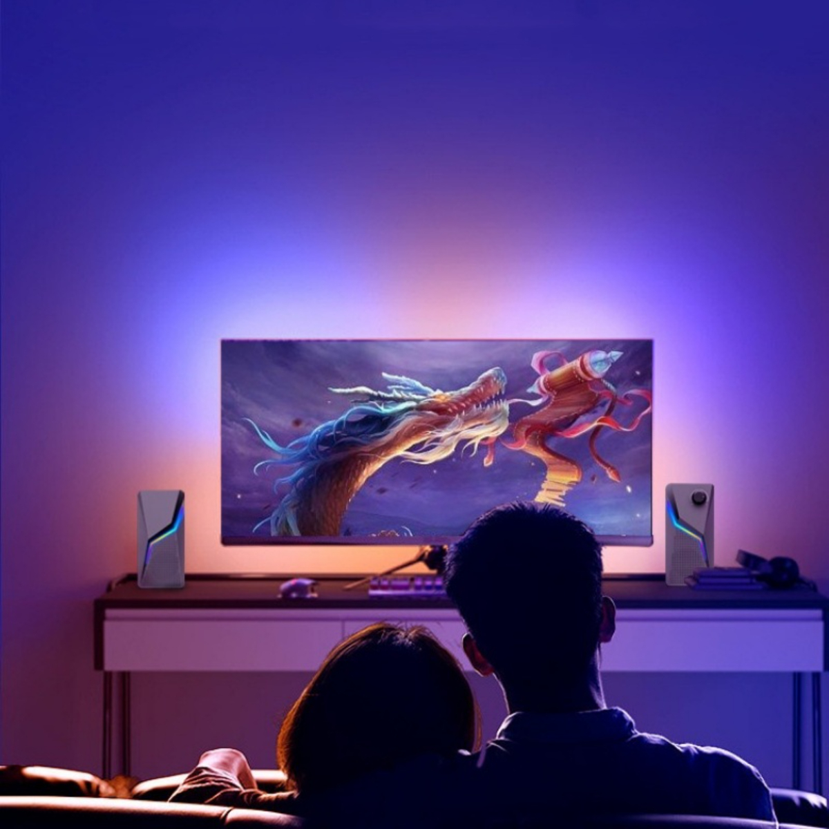 Ein Paar schaut fern mit einer Drachen-Grafik auf dem Bildschirm, mit zwei Lautsprechern auf beiden Seiten des Fernsehers.