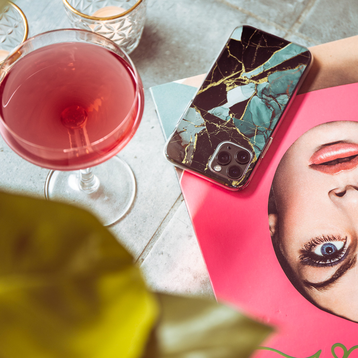 Verre à cocktail avec boisson rouge. Coque de téléphone sur un magazine avec visage de femme.