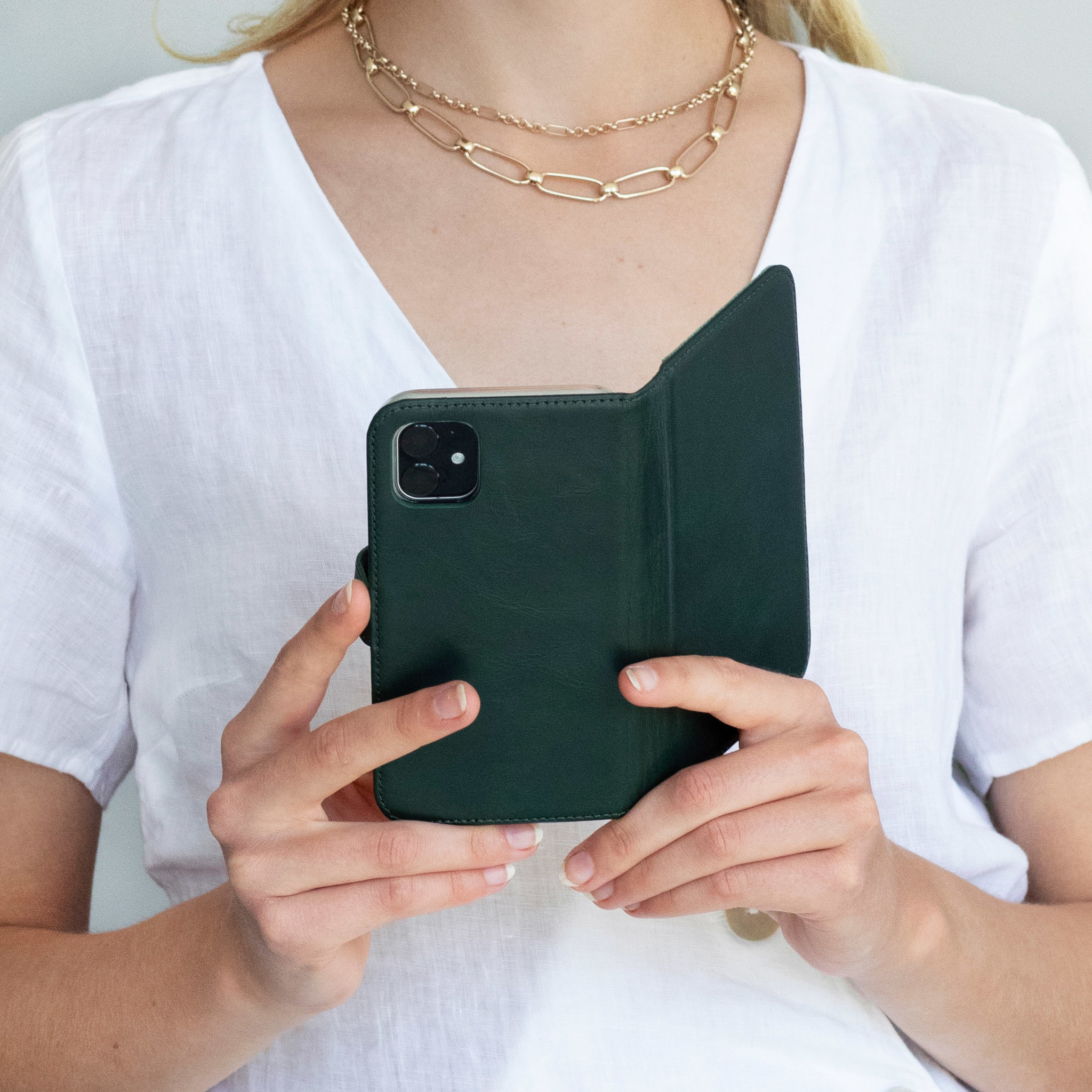 Femme tenant un étui de téléphone vert ouvert. Elle porte une chemise blanche et une chaîne dorée.
