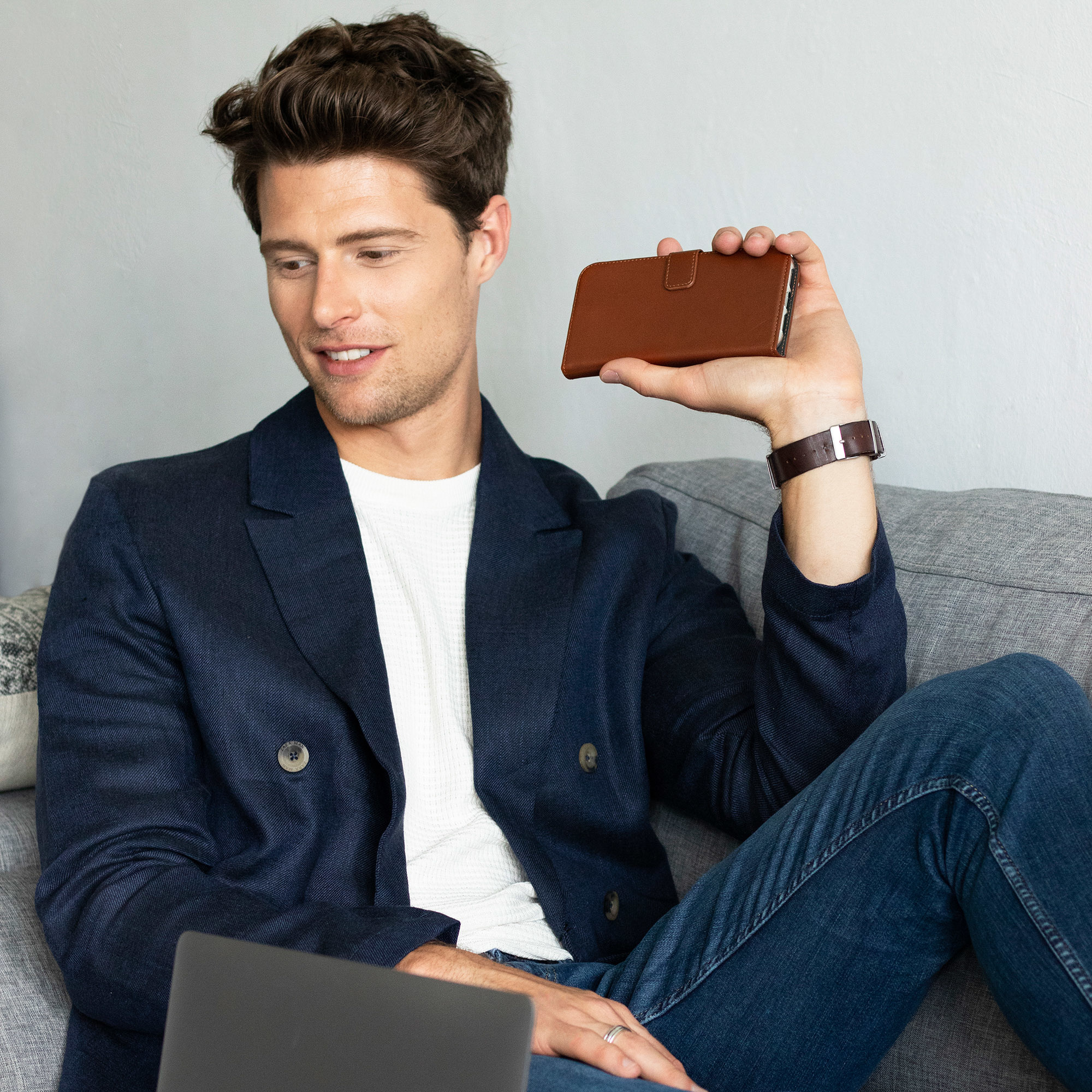 Un homme assis sur un canapé tient un étui de téléphone marron, avec un ordinateur portable.