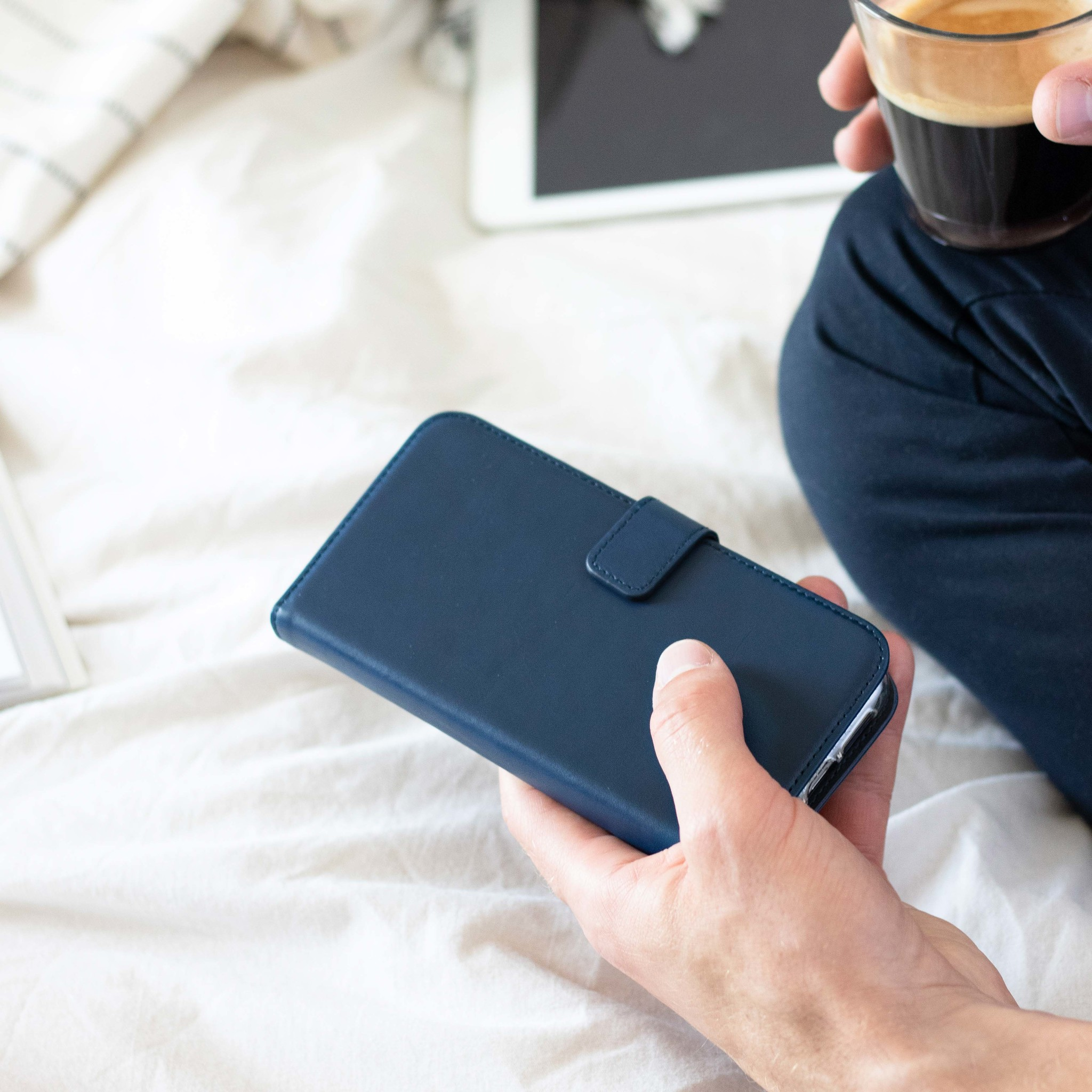 Une main tenant un étui de téléphone bleu avec un téléphone sur un lit.