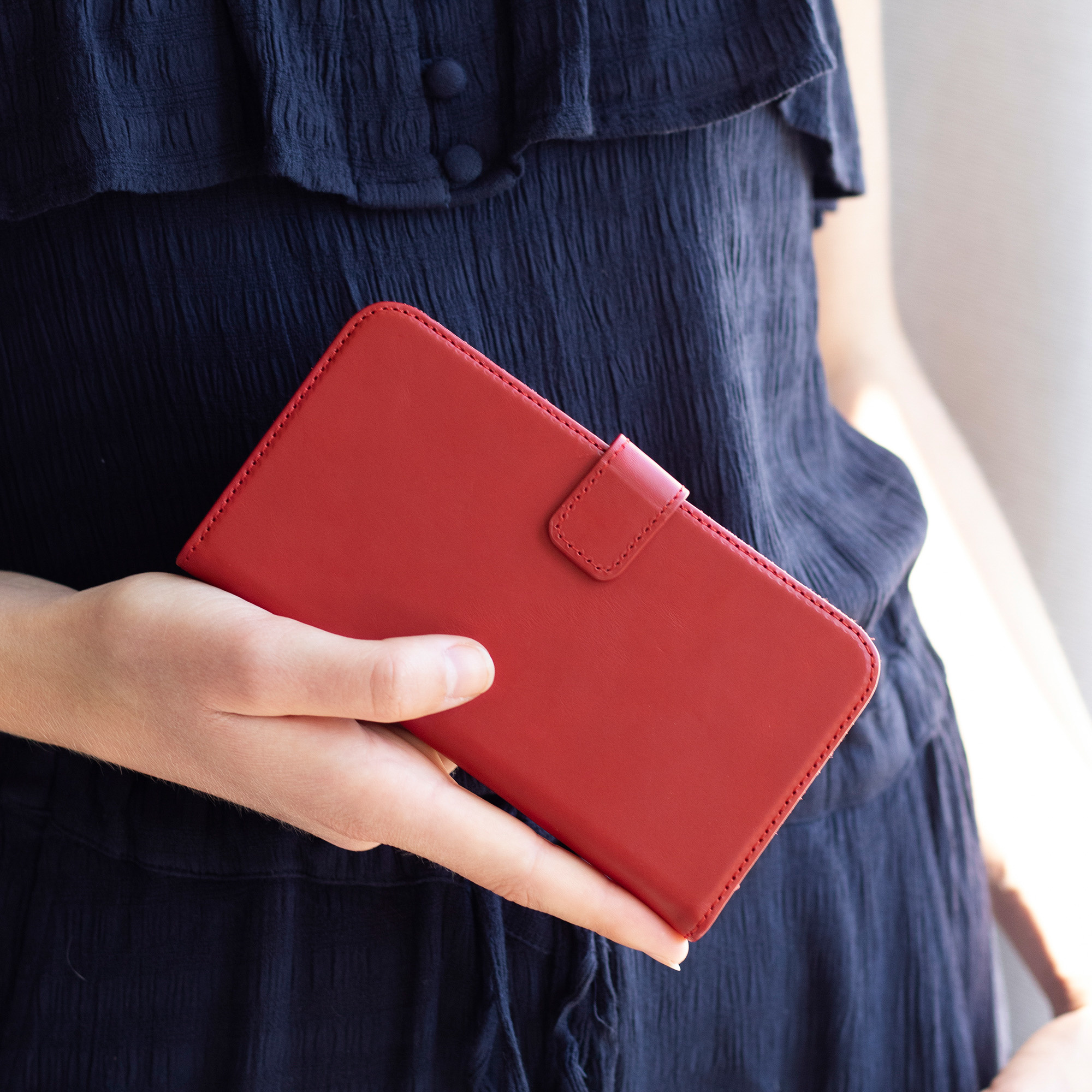 Une personne tenant un étui de téléphone en cuir rouge, avec une robe bleu foncé en arrière-plan.