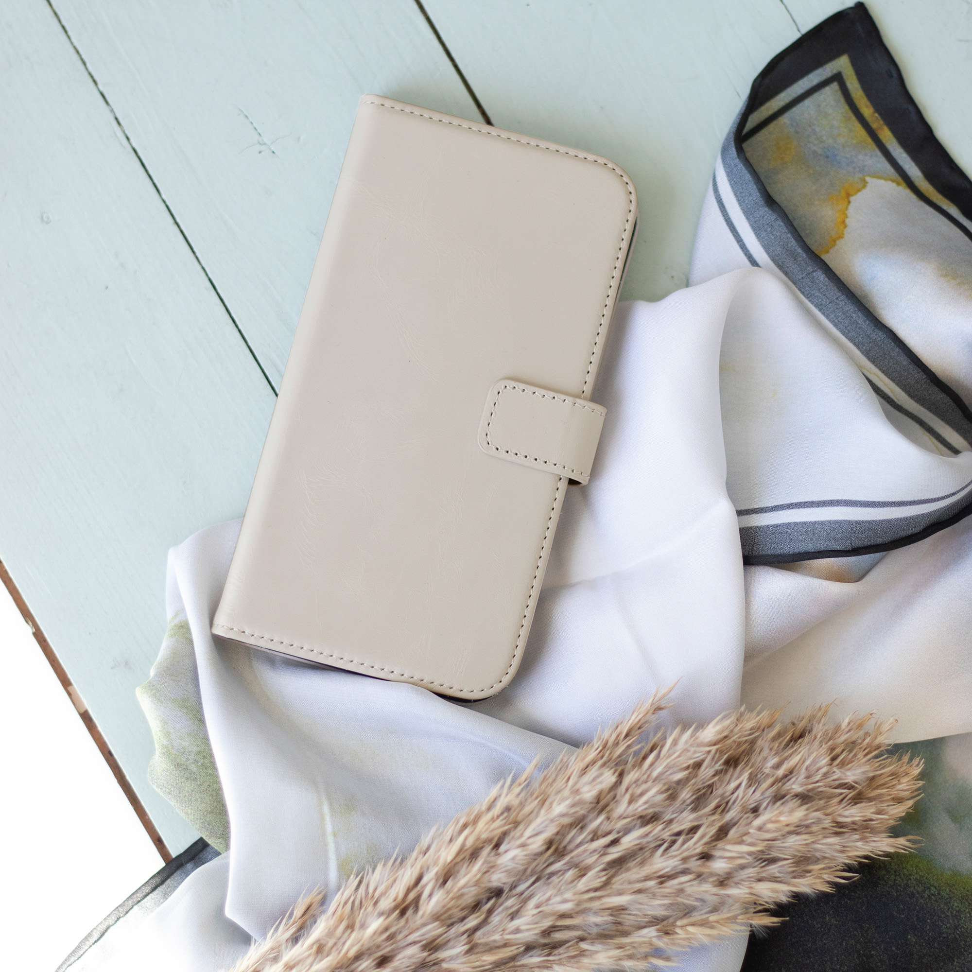 Étui de téléphone beige, fermé. Sur un tissu blanc et une surface bleu clair.