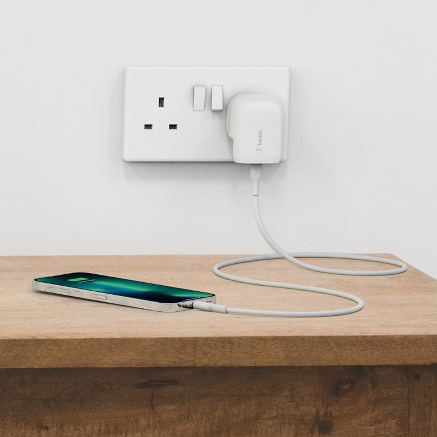 Un telefono è in carica accanto a una presa a muro. Un caricabatterie è collegato e il telefono è appoggiato sul legno.