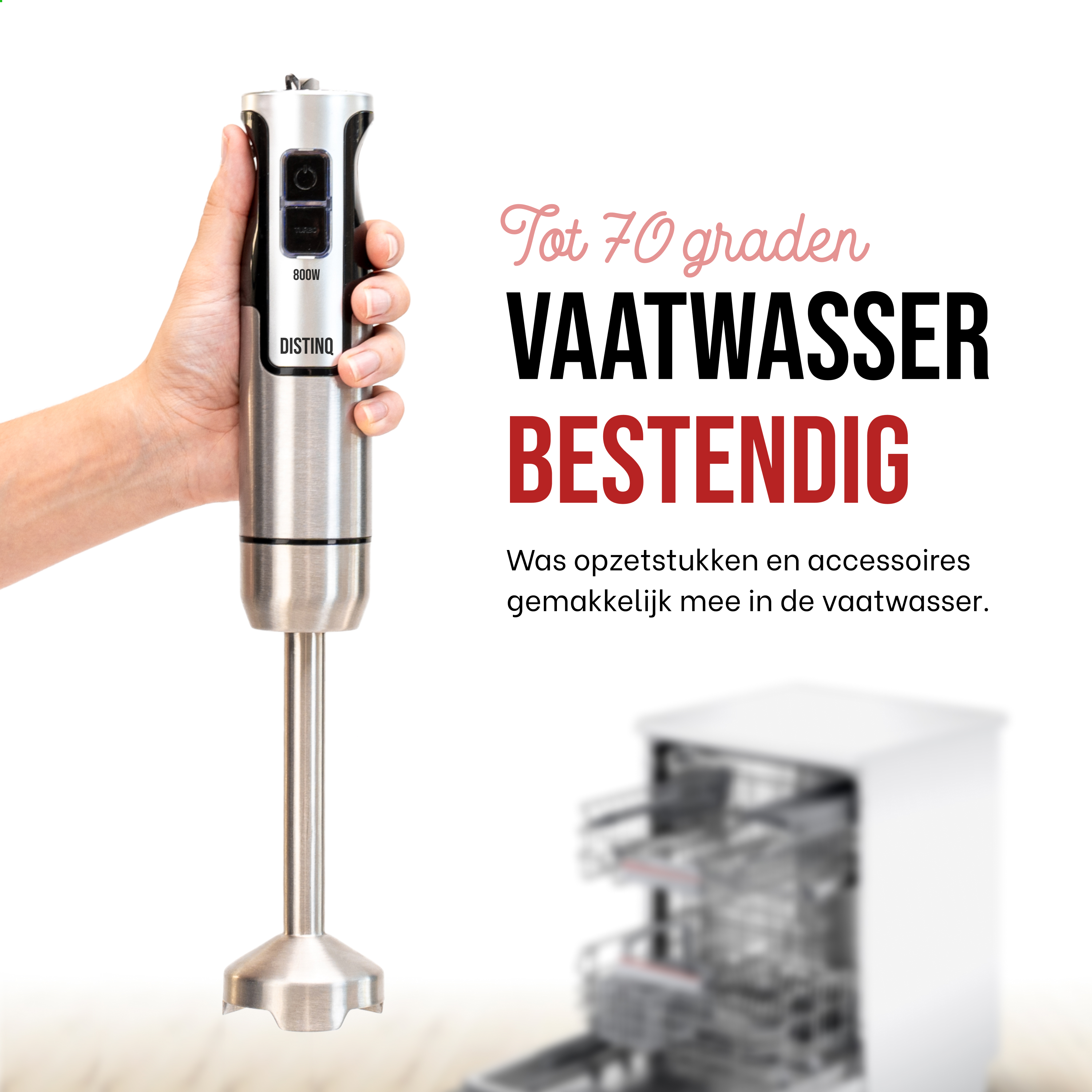 A silver hand blender with a hand holding it. A dishwasher is blurred in the background.