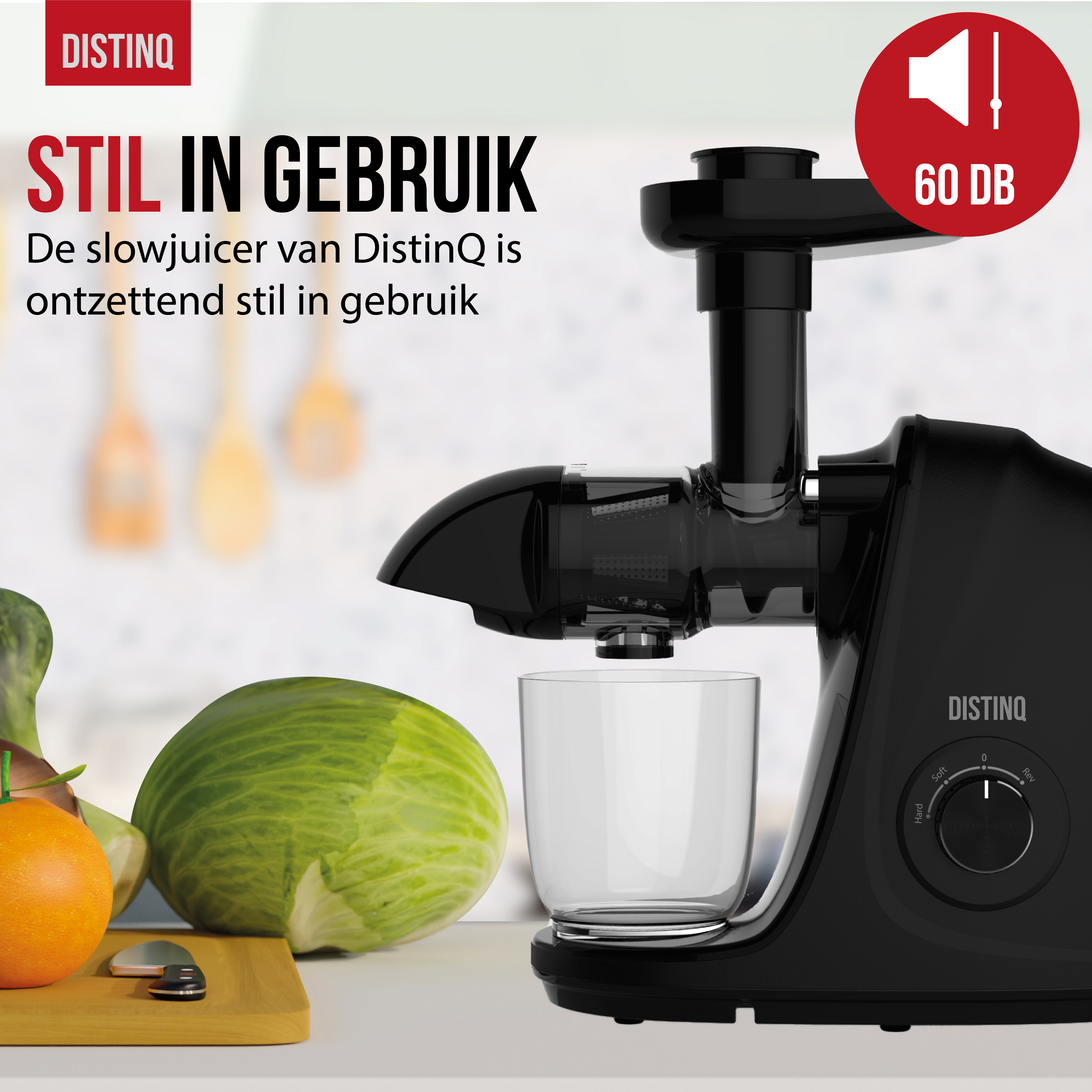 A black juicer with a glass, an orange, and a green cabbage on a wood table.