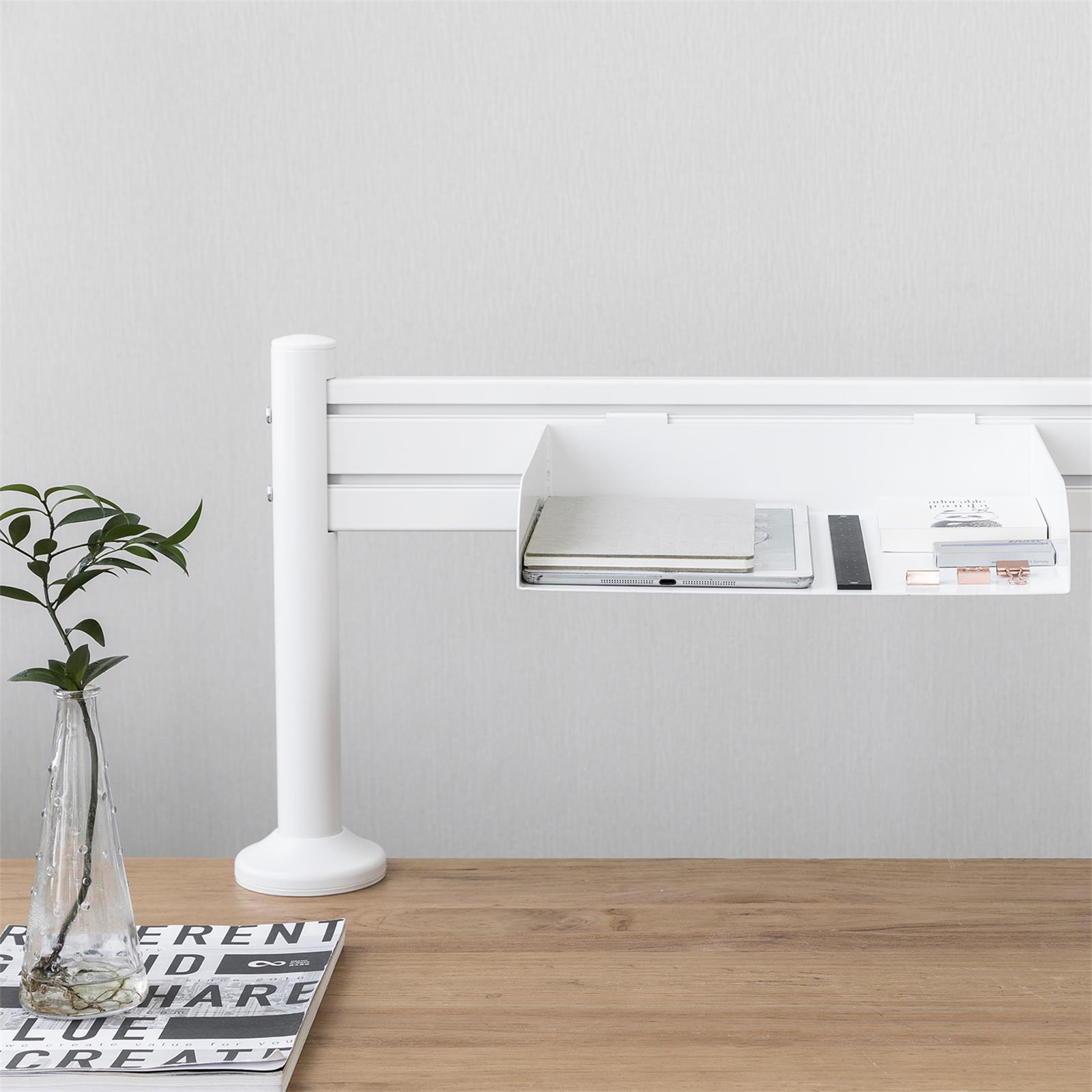 Una configuración de escritorio blanca con una planta, revista y estante con laptop.