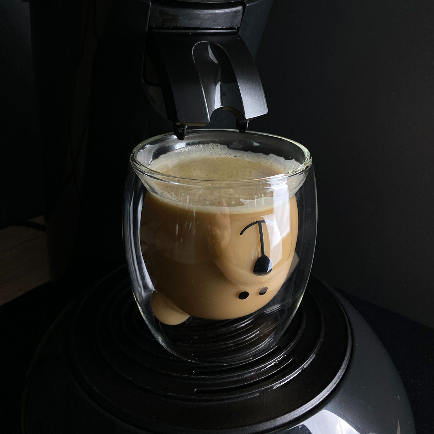 Kaffee in einem bärenförmigen Glas mit einer schwarzen Kaffeemaschine.